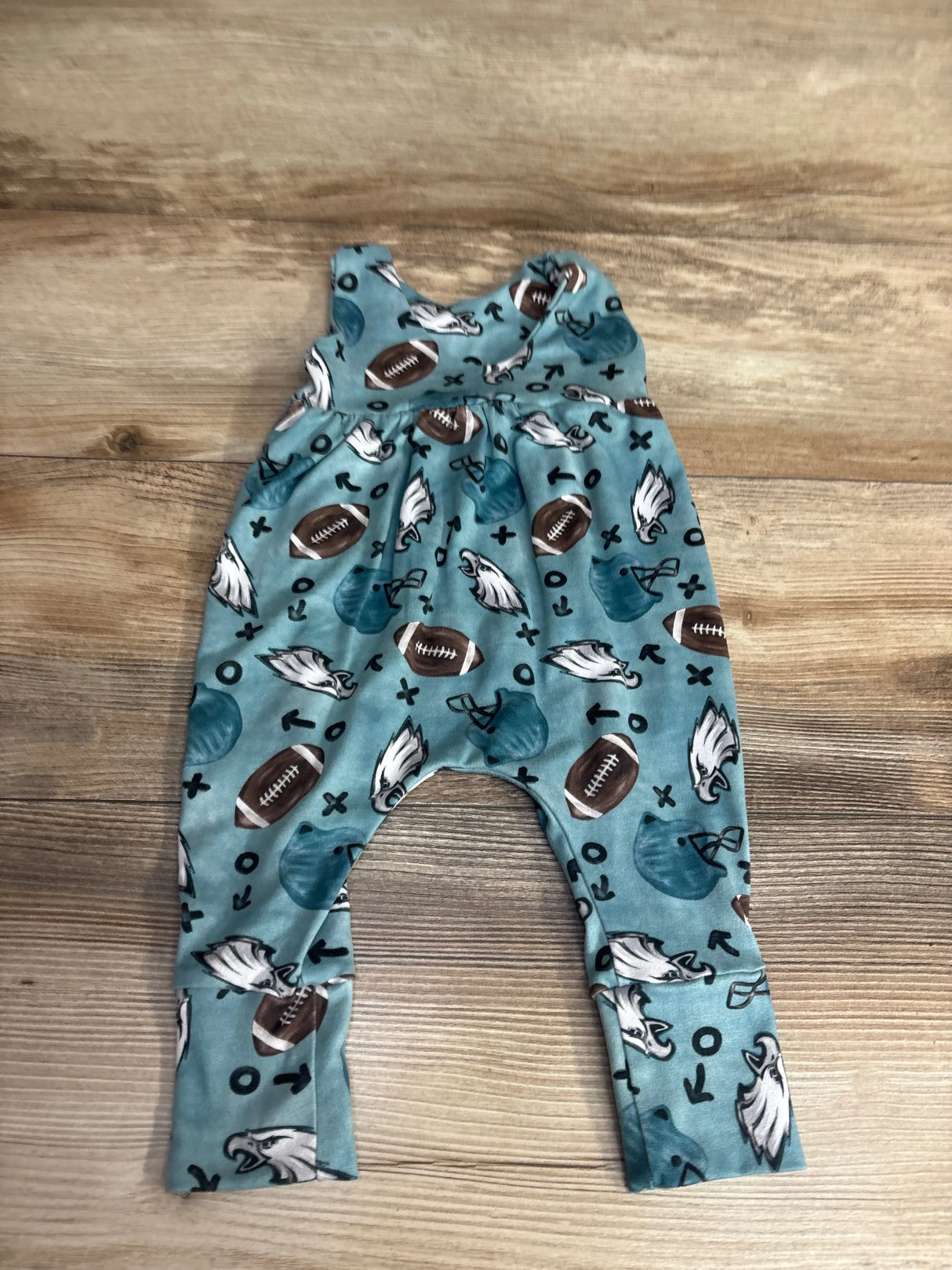 Blue baby romper with football, eagle, and play pattern, laid flat on wood background