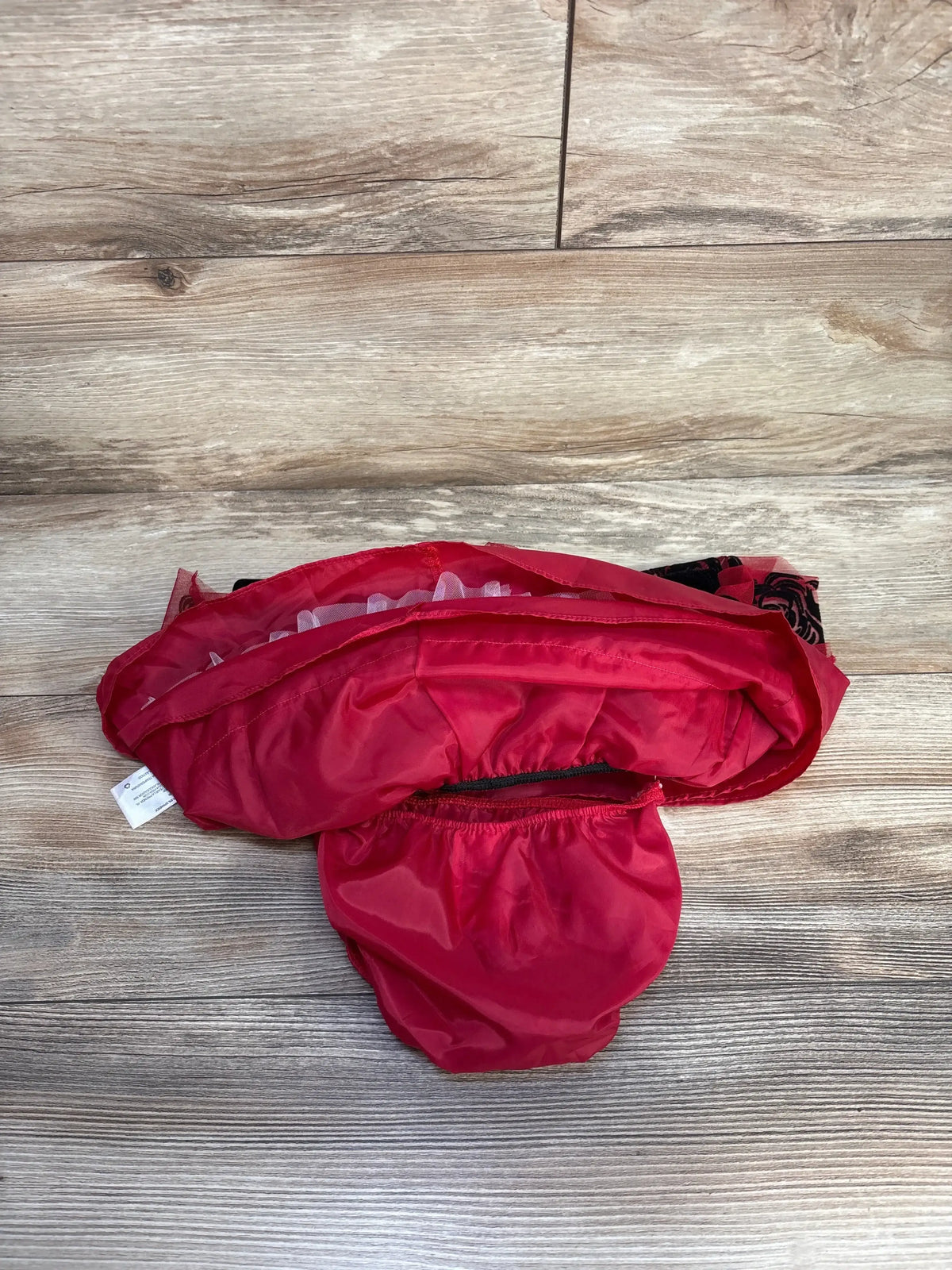 Top view of red baby bloomers with elastic leg openings and red tulle and black rose-pattern lining on wooden floor