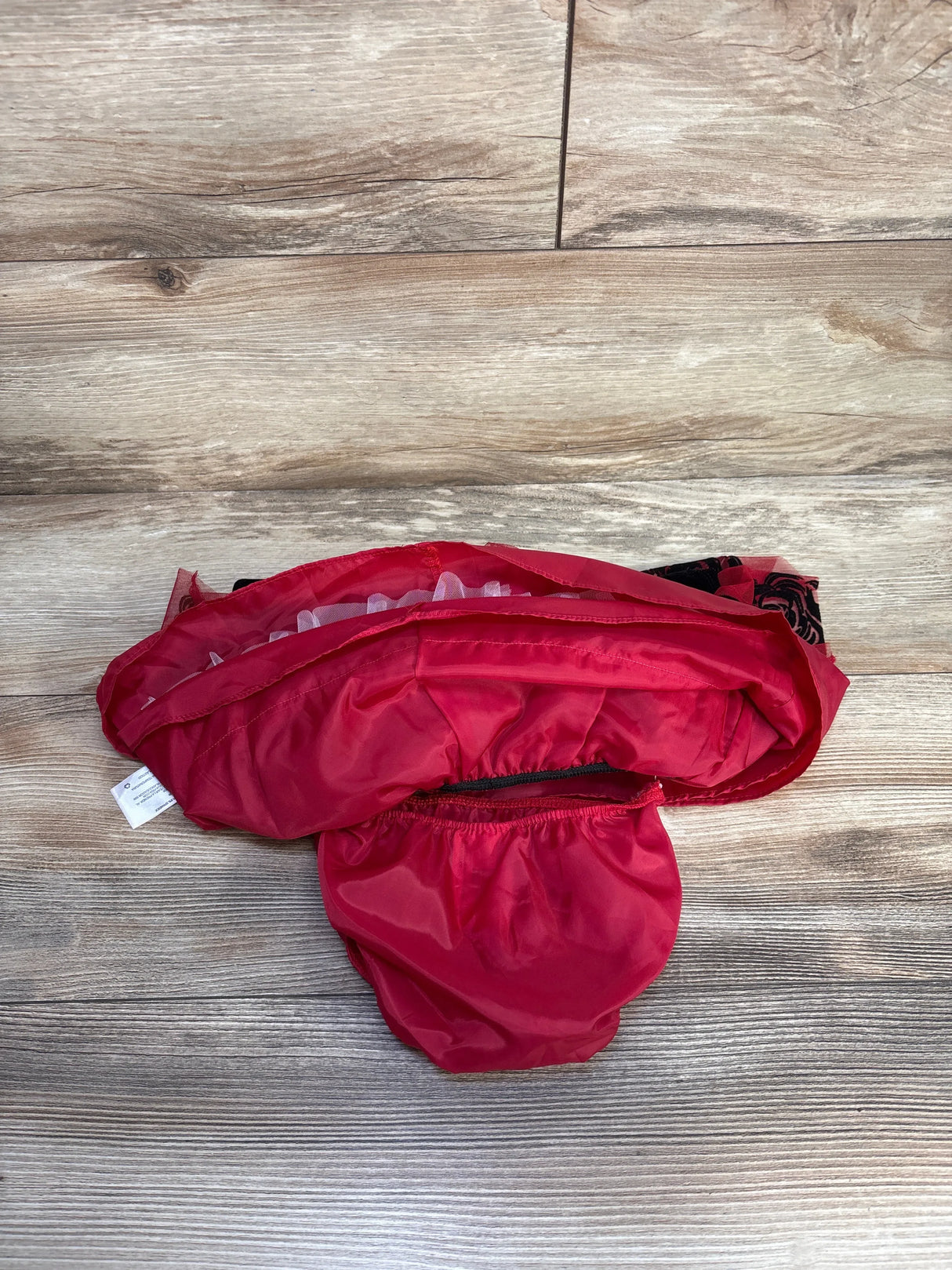 Folded red fabric pet diaper on wooden floor with black and red rose pattern