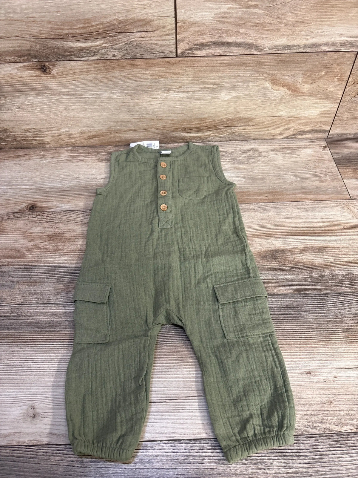 Flat lay of green sleeveless henley jumpsuit (6 to 12 months) showing wooden buttons, chest and cargo pockets on wood background