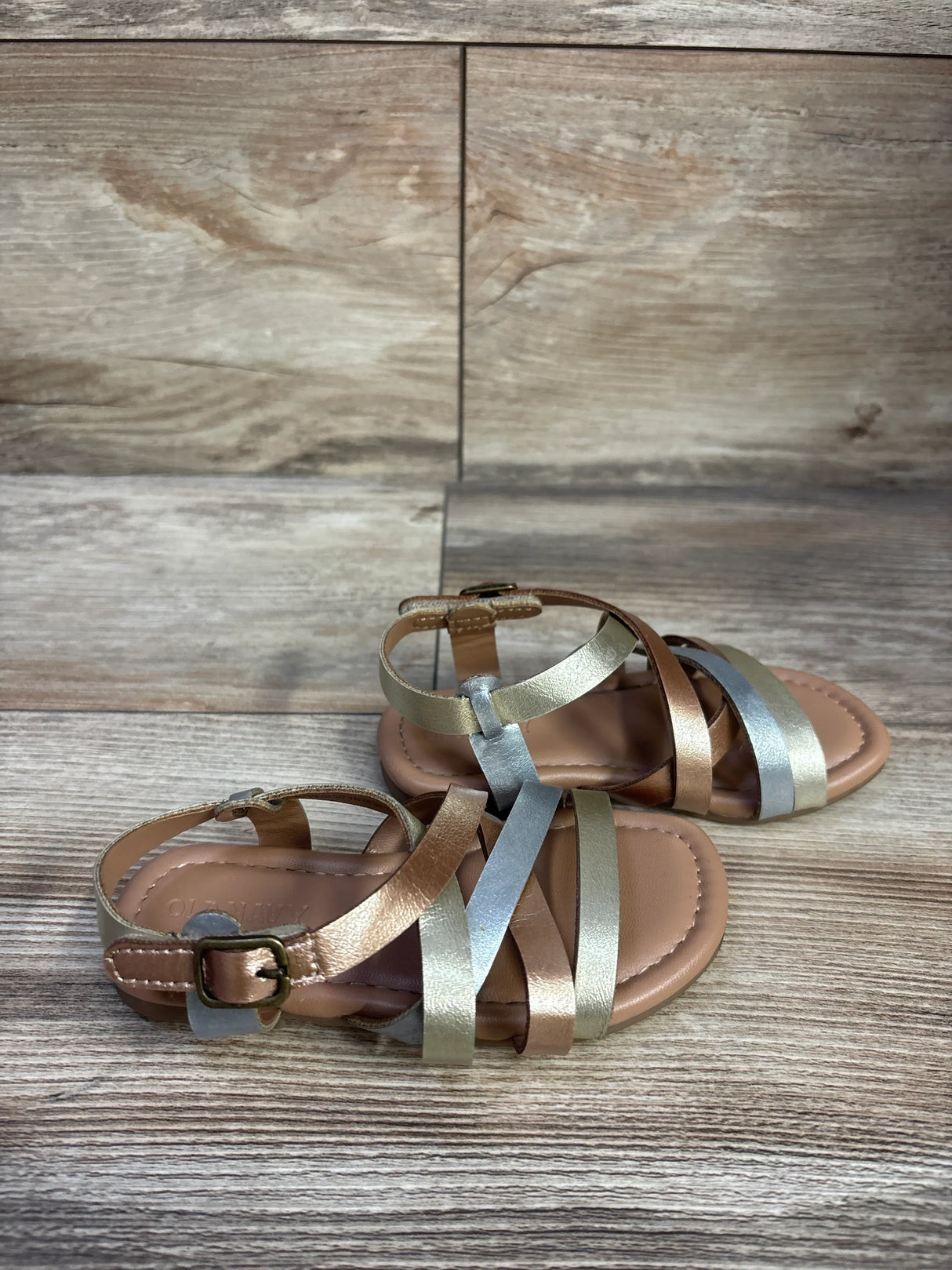 Angled view of Old Navy metallic strappy sandals, bronze and silver straps, ankle buckle on wood background, size 7C