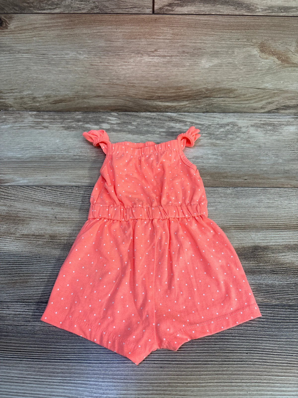 Flat lay of coral polka dot shortie romper showcasing ruffled straps and shorts on a wood-grain background