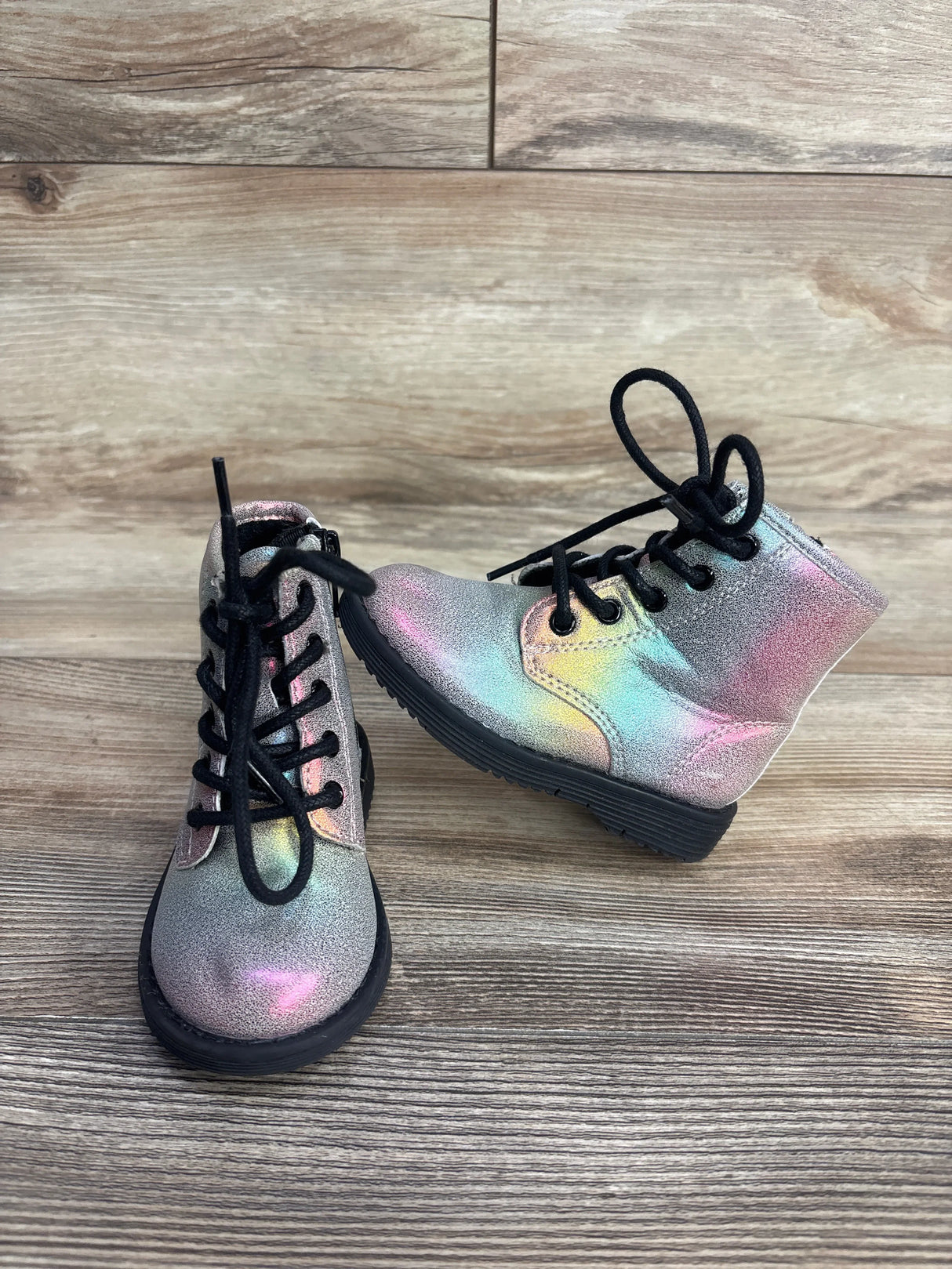 Iridescent lace-up kids boots with black soles on wood background