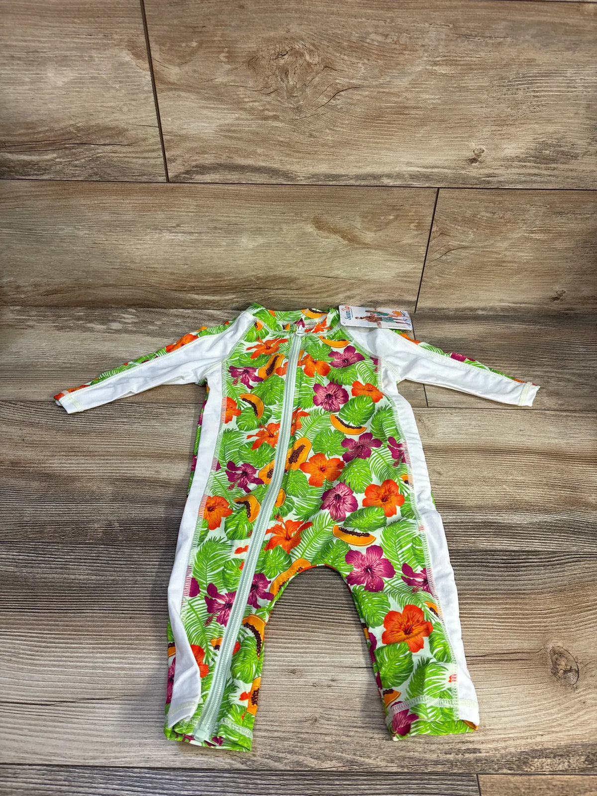 Front view of SwimZip long sleeve romper sunsuit showcasing hibiscus green floral print and full-length zipper on wood floor