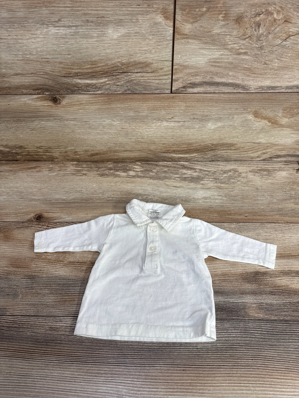 White long sleeve baby shirt with buttons and collar on wooden background