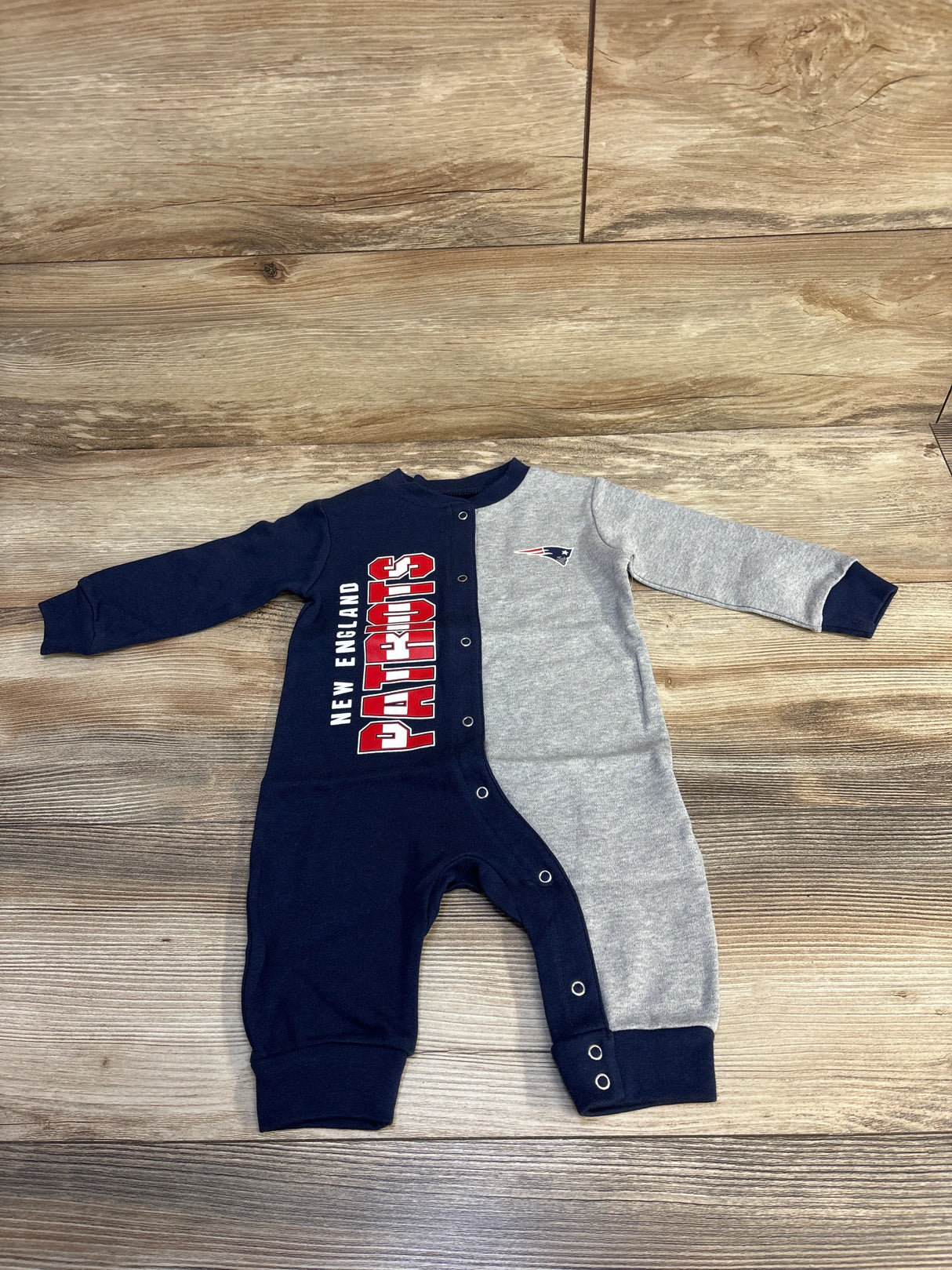 New England Patriots baby romper with navy blue and gray colors, snap buttons, and team logo on wooden floor