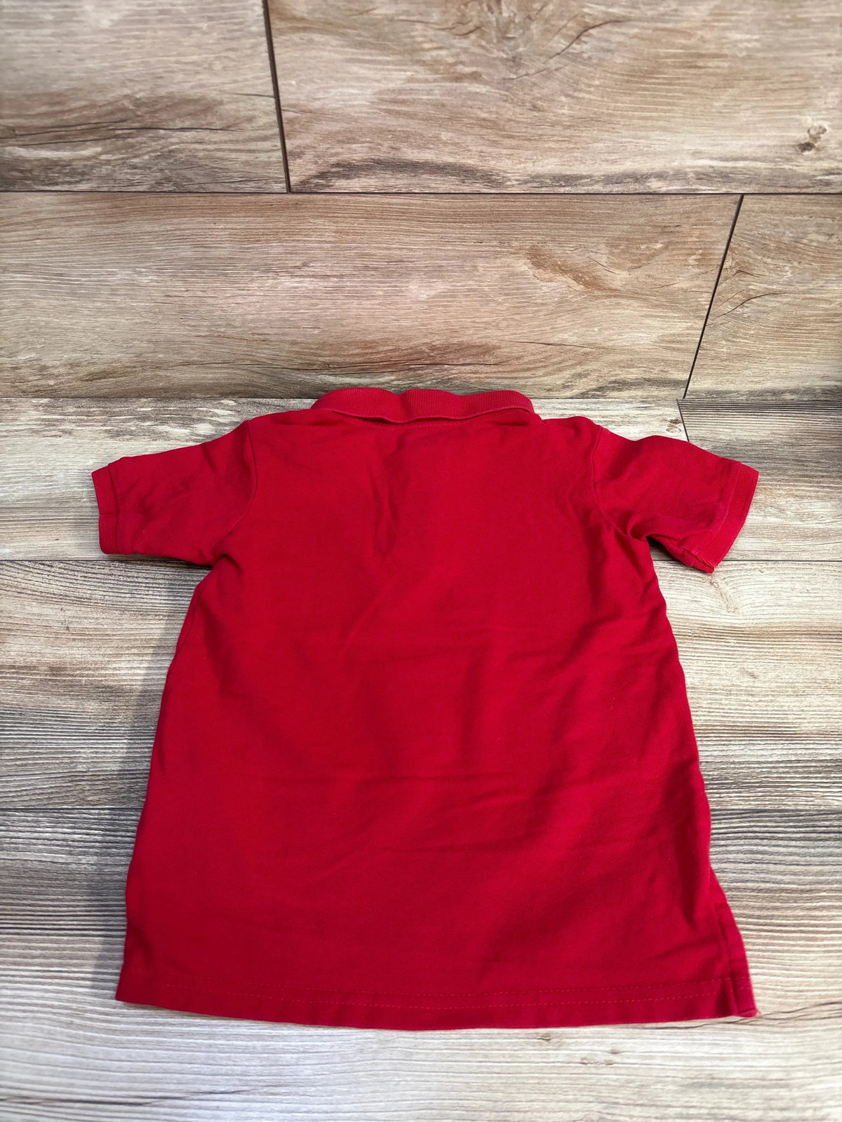 Back view of red toddler polo shirt showing ribbed collar and short sleeves on wood floor