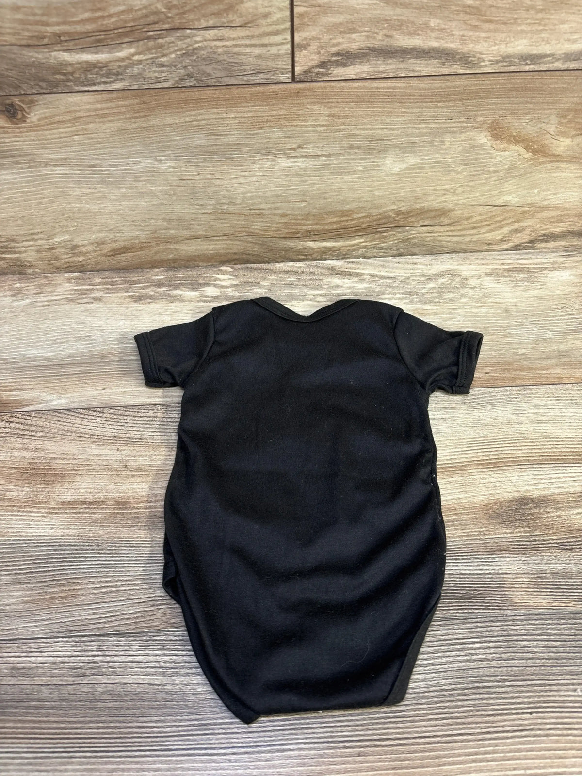 Back view of I’m Turtley Cute black bodysuit (3-6 months) showing short sleeves and envelope neckline, flat-laid on wood floor background