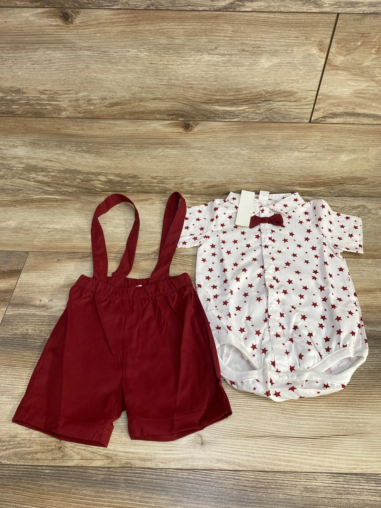 Baby boy outfit with red suspender shorts and white star print onesie on wood floor