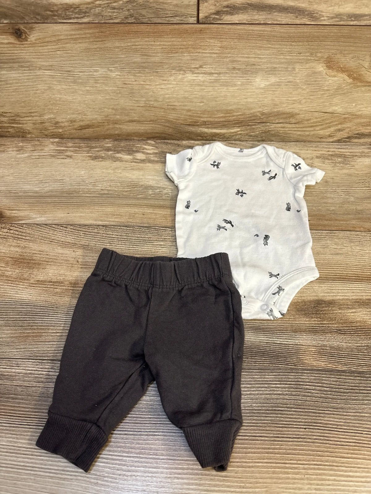 White baby bodysuit with animal print and black pants set on wood floor