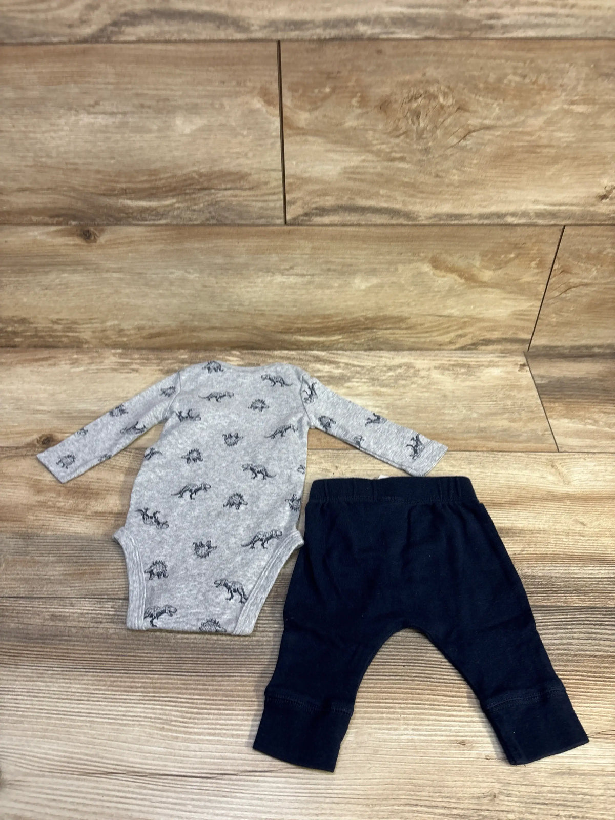 Flat lay of Carter’s grey long-sleeve bodysuit showcasing dinosaur print and black pants on wood surface