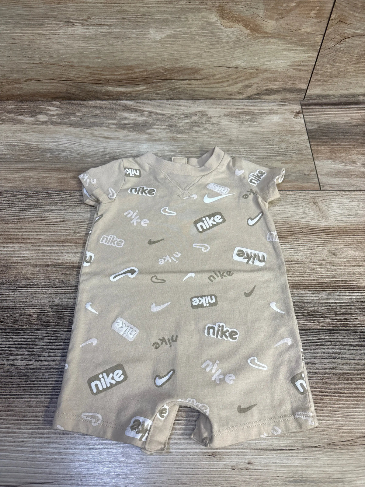 Beige baby romper with white Me n Mommy To Be logo patterns on a wooden background