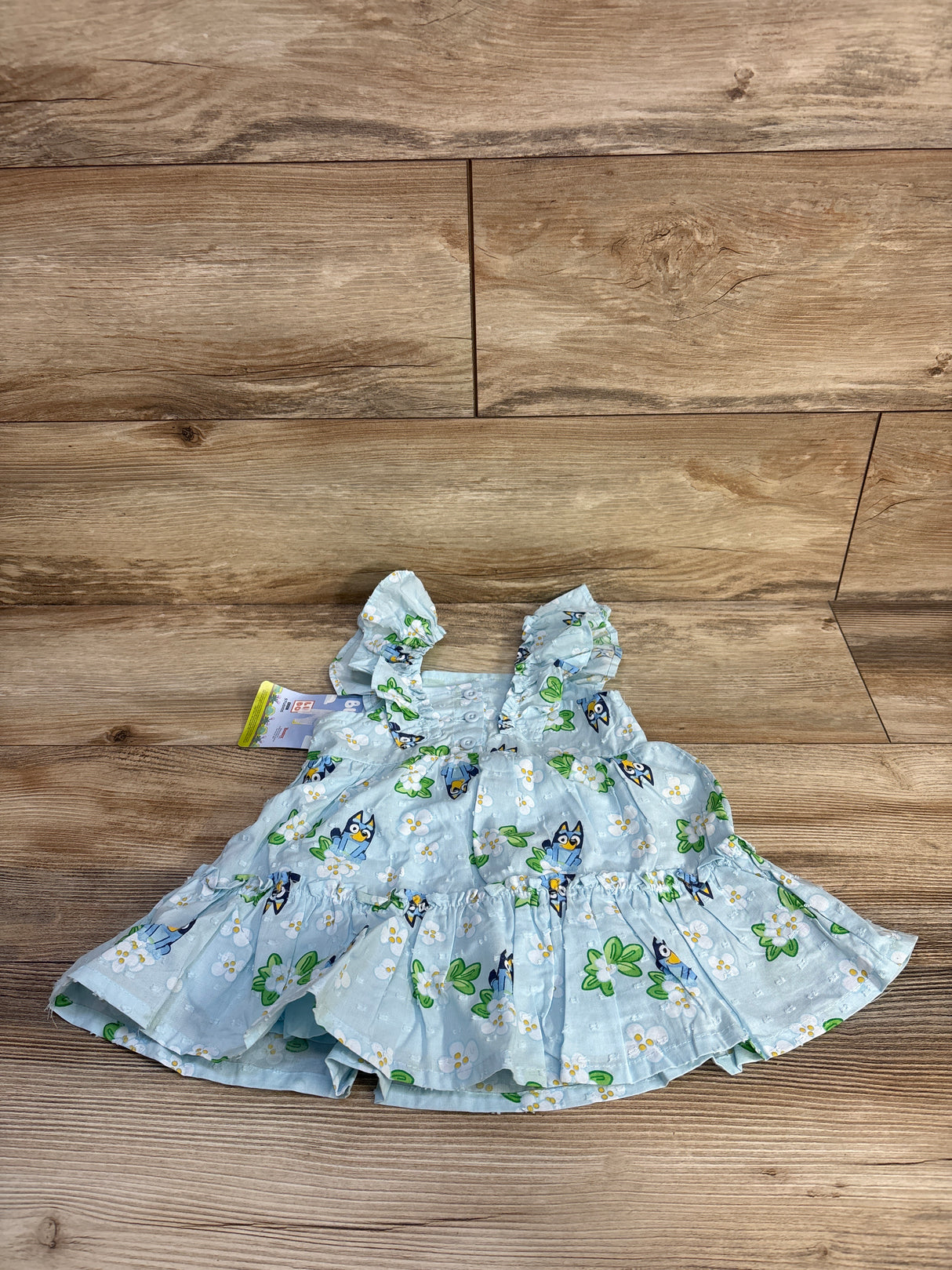 Top down view of light blue Bluey floral baby dress size 12 months showcasing Swiss dot texture, ruffled skirt on wood floor background