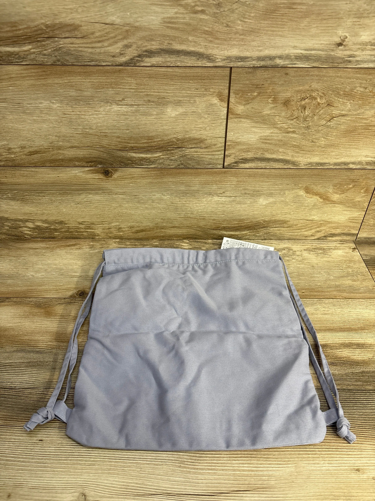 Front view of NEW Disney Princess Drawstring Bag showcasing light gray fabric and knotted drawstring straps on wood-grain background