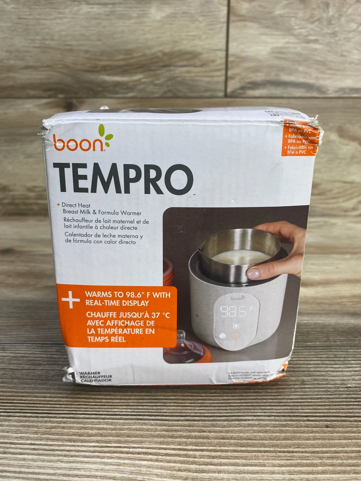 Front view of Boon Tempro breastmilk warmer box showing digital 98.6 F display and orange label on wooden tabletop
