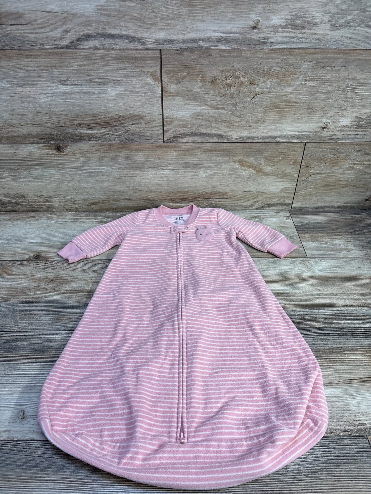 Front view of Carter’s pink 3-6m blanket sleep sack with white stripes, long sleeves, zipper, and bear patch on wood background