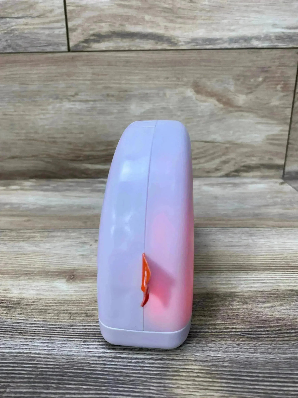Side view of Fisher-Price Soothe & Glow Rainbow sound machine showing pink glow and orange clip on wood background