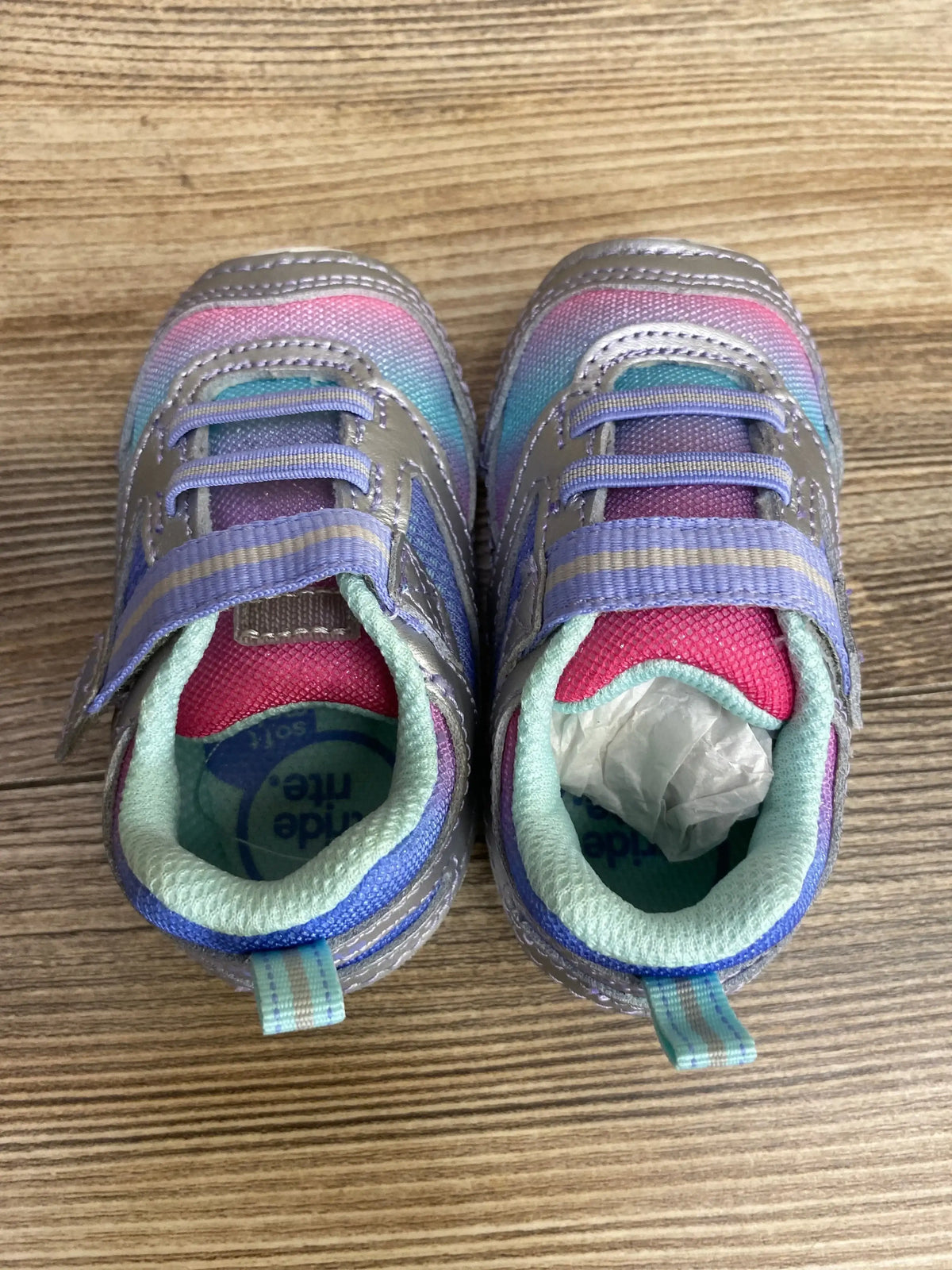 Pair of pastel rainbow toddler sneakers with Velcro straps on a wood floor
