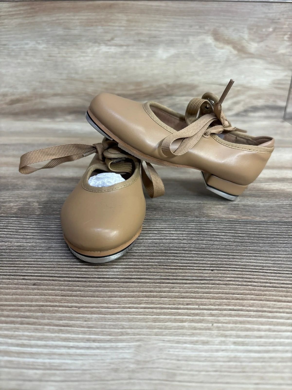 Tan kids’ tap dance shoes with ribbons and metal taps on wooden floor