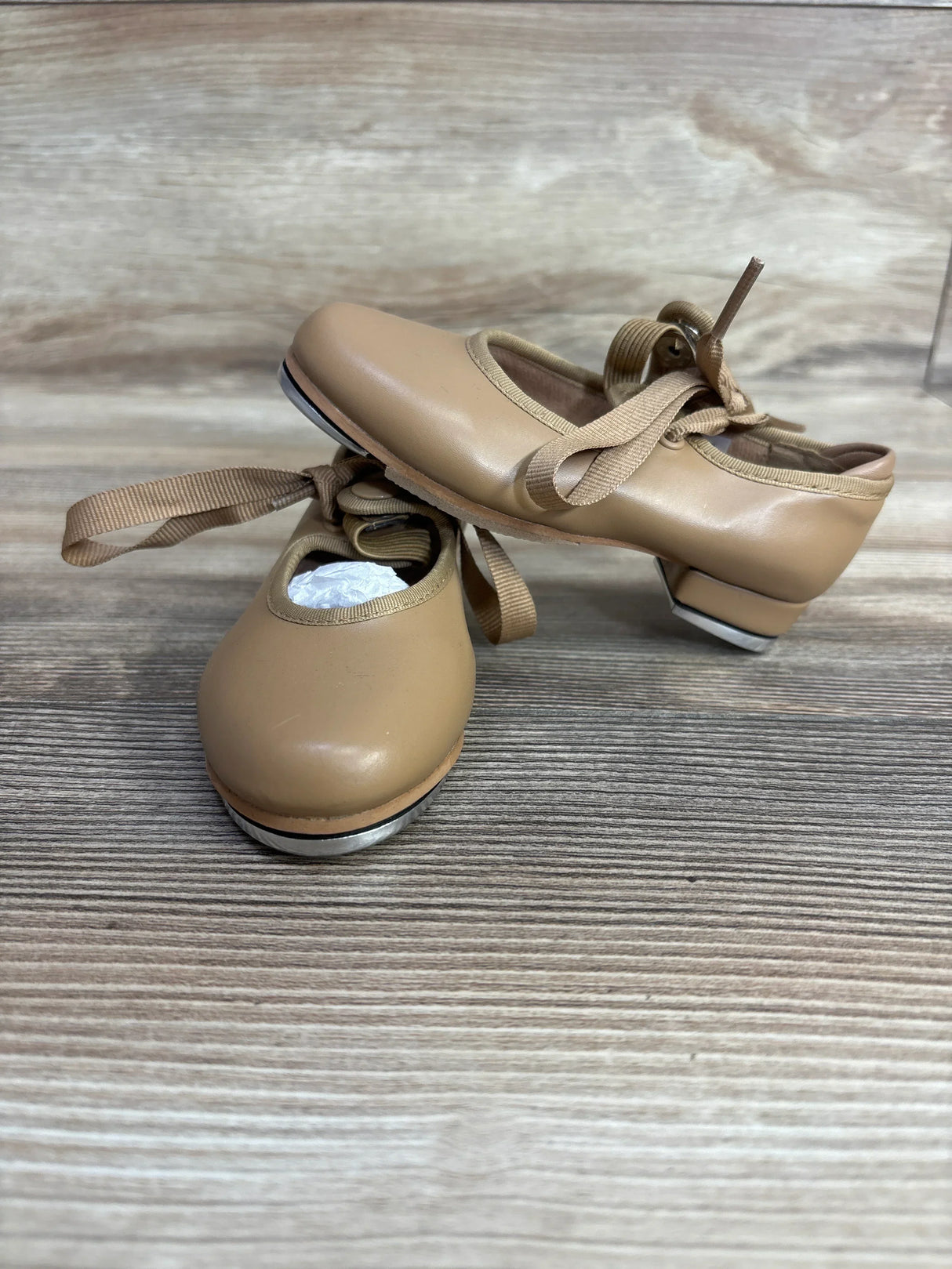 Tan kids’ tap dance shoes with ribbons and metal taps on wooden floor
