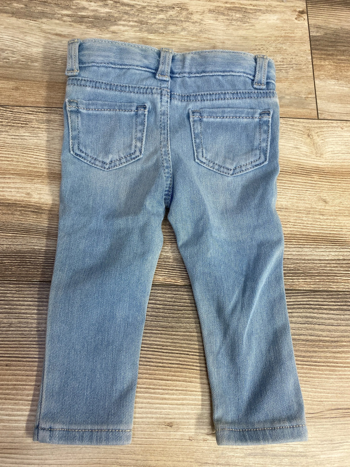 Back view of light blue toddler jeans with two pockets on wooden floor