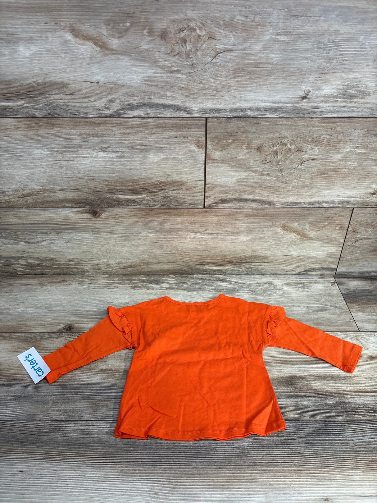 Bright orange Carter's long sleeve baby top with ruffle sleeves, laid flat on wood floor