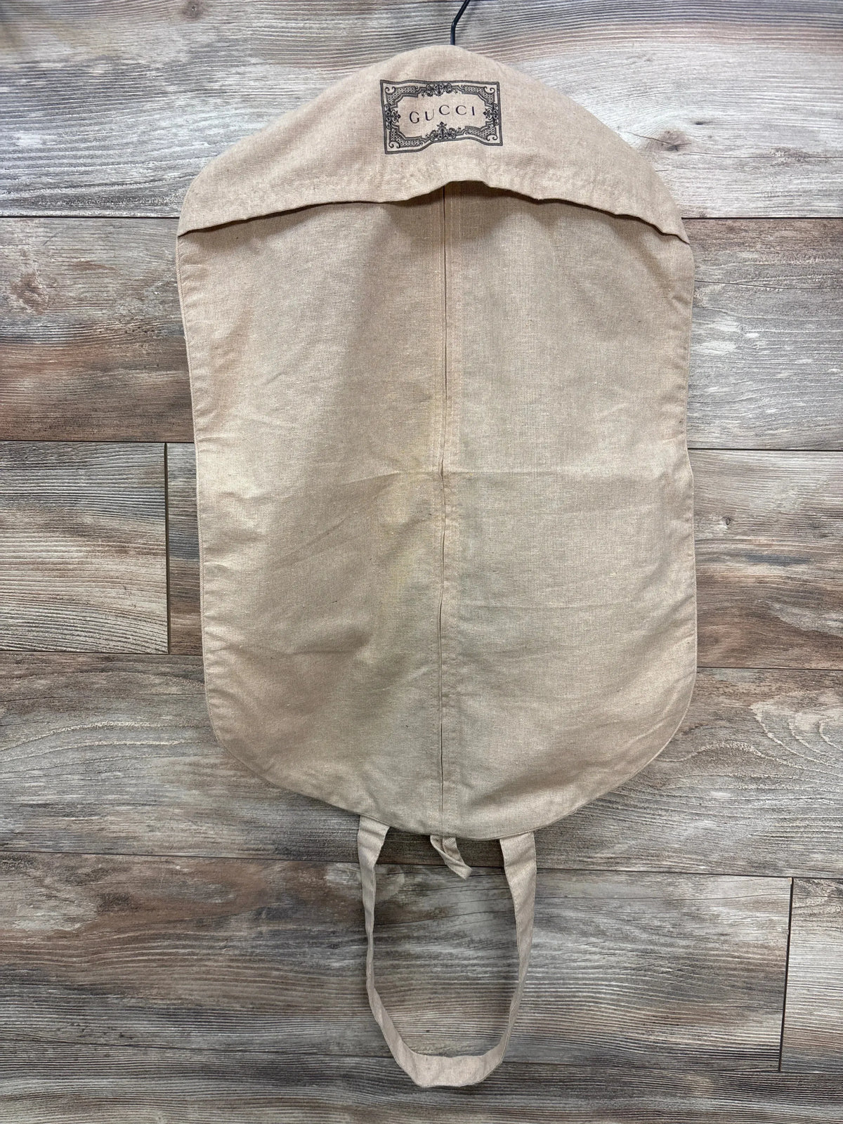 Front view of Gucci garment bag showcasing its embroidered logo on a wood floor