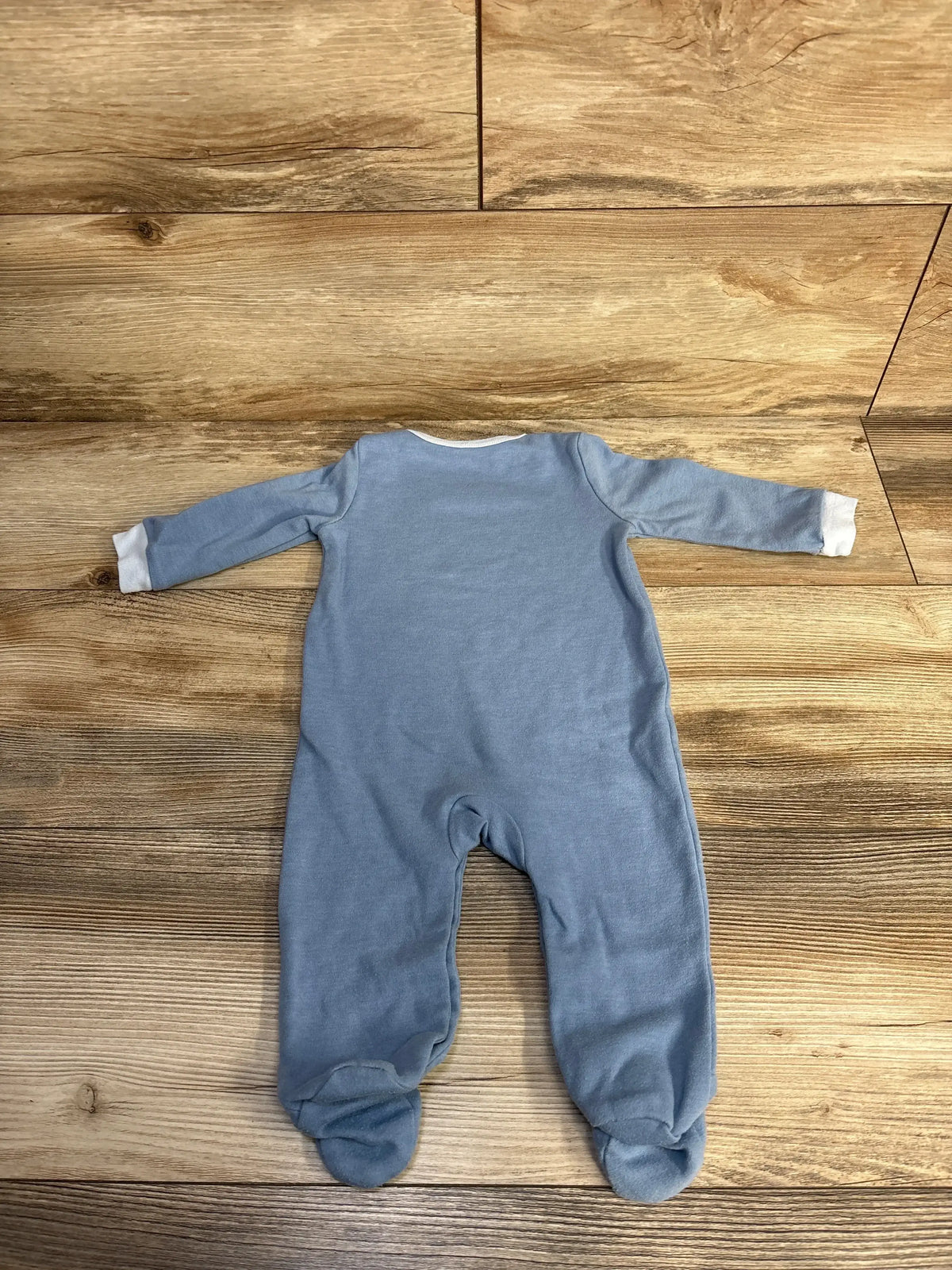 Blue long-sleeve footed baby onesie with white cuffs on wooden floor