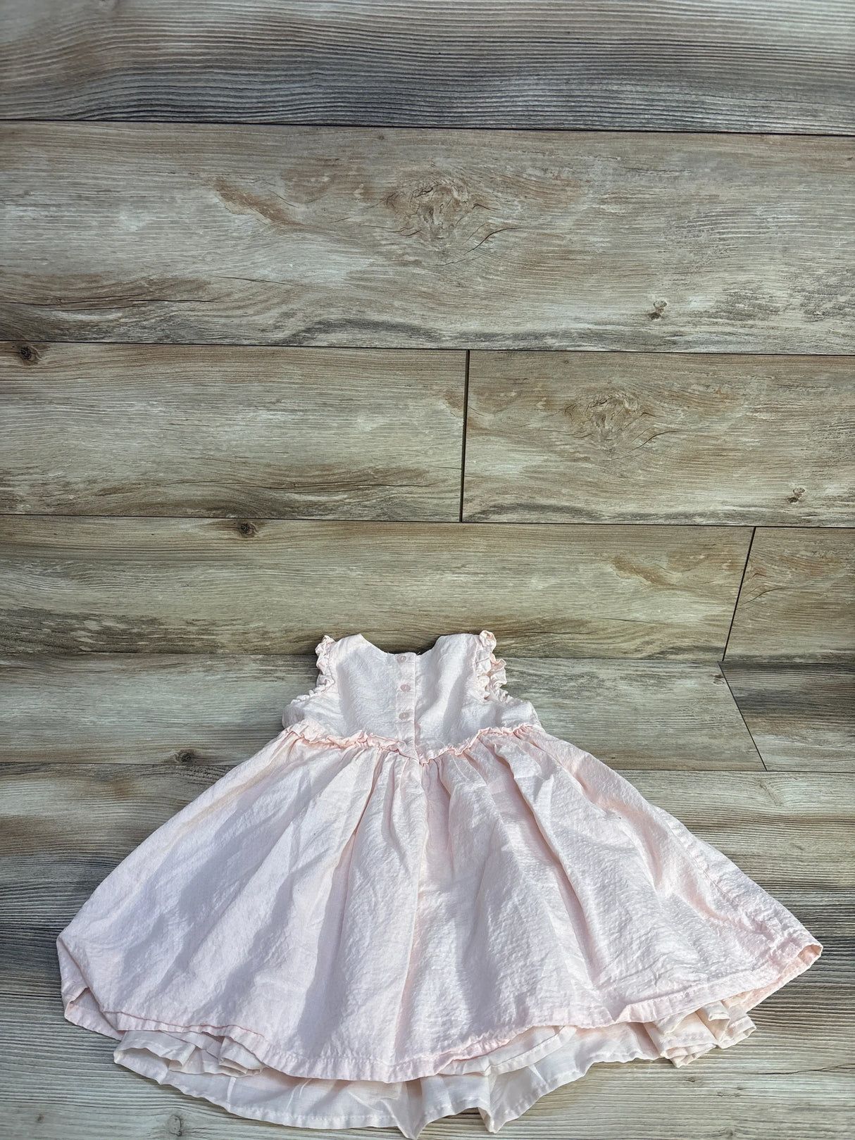Front flat lay of pink toddler dress size 4T showing ruffled cap sleeves, gathered skirt with layered hem on light wood floor
