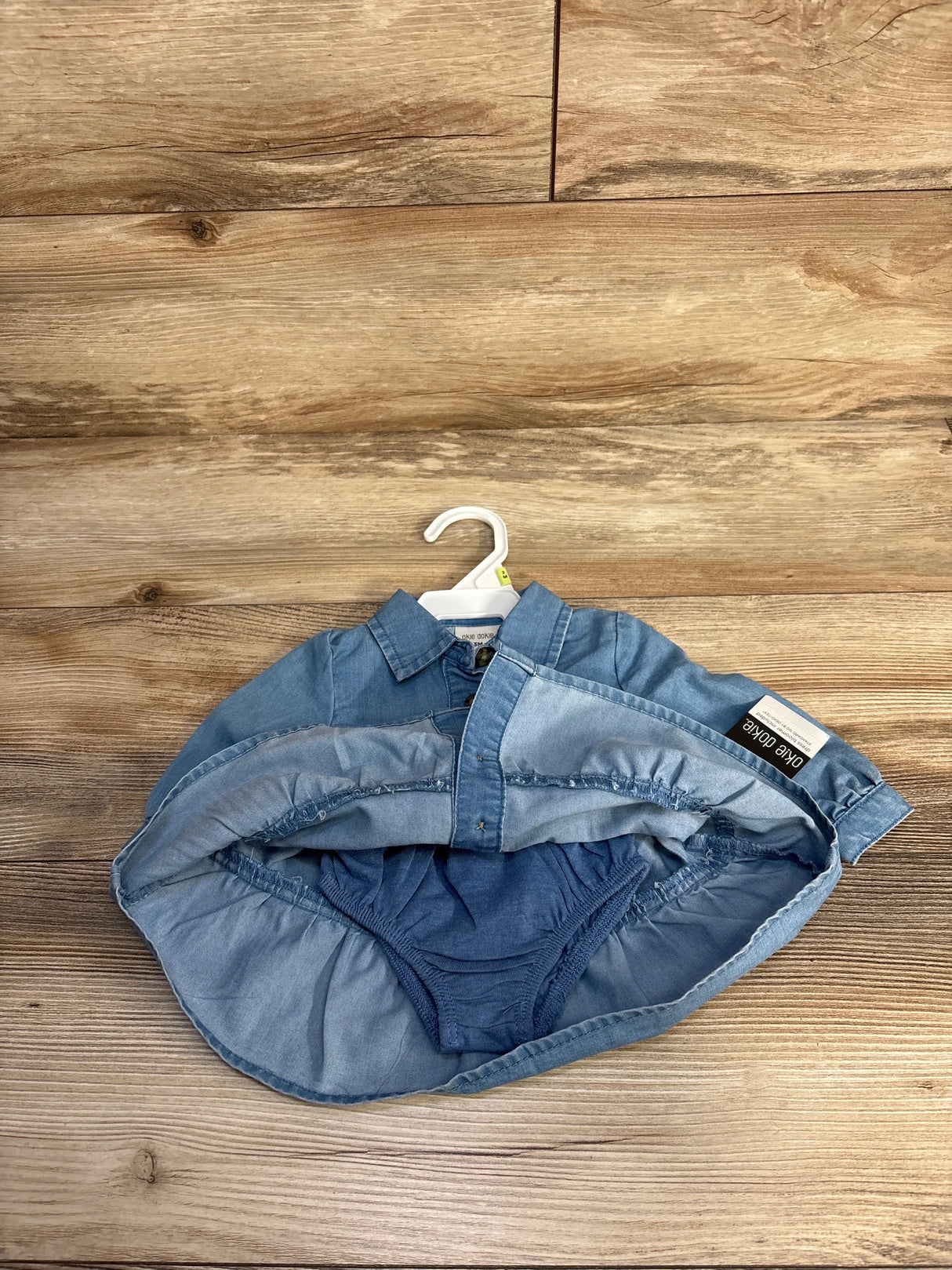 Blue baby dress with attached diaper cover on hanger against wood background
