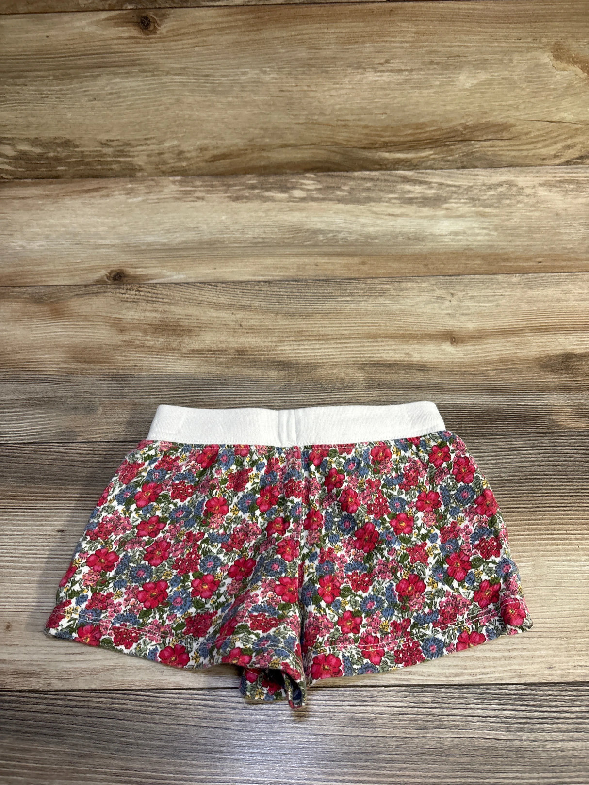 Flat lay of Polo Ralph Lauren spa terry shorts (size 4T) showcasing white elastic waistband and red-pink floral print on wood background
