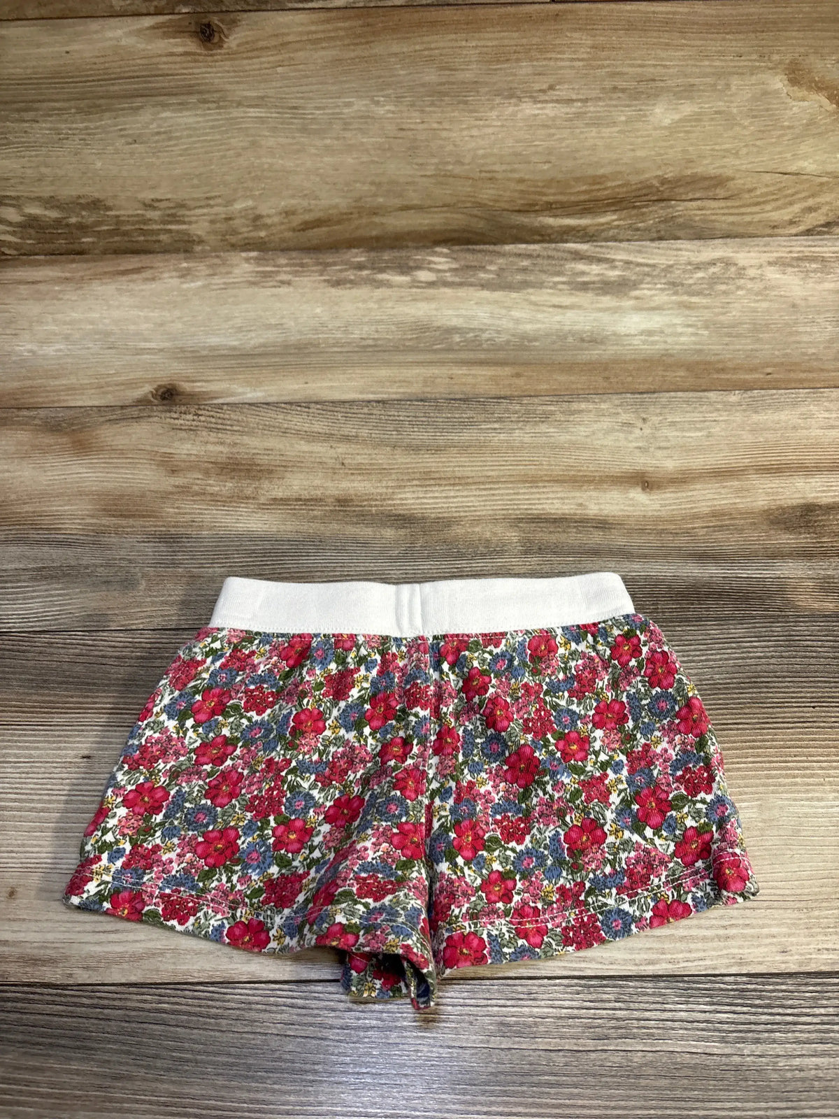 Flat lay of Polo Ralph Lauren spa terry shorts (size 4T) showcasing white elastic waistband and red-pink floral print on wood background