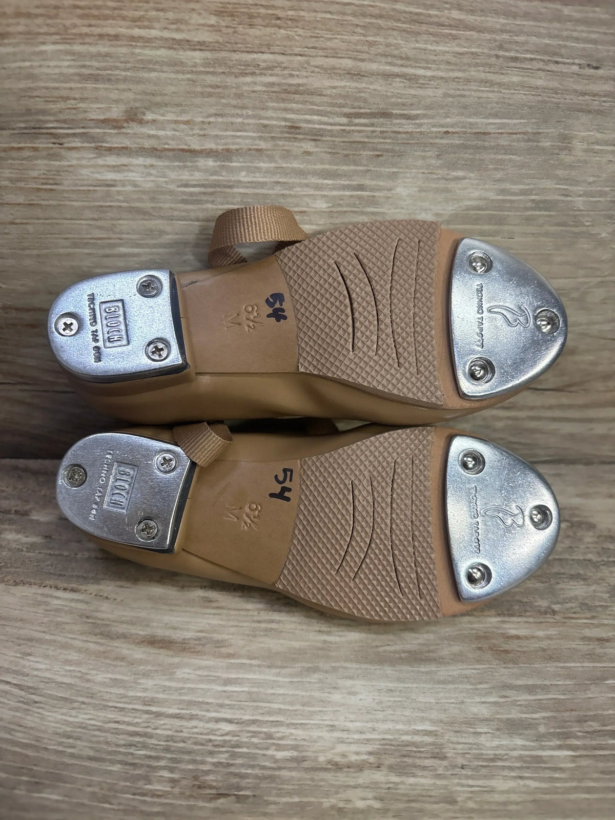Bottom view of Bloch Annie Tyette tan children's tap shoes showing metal toe and heel taps and visible size 6½ marking on wooden floor