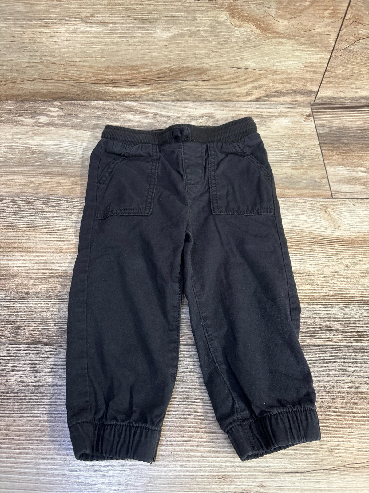 Front view of Jumping Beans black drawstring joggers in size 18 months showcasing front pockets and elastic cuffs on a wood floor