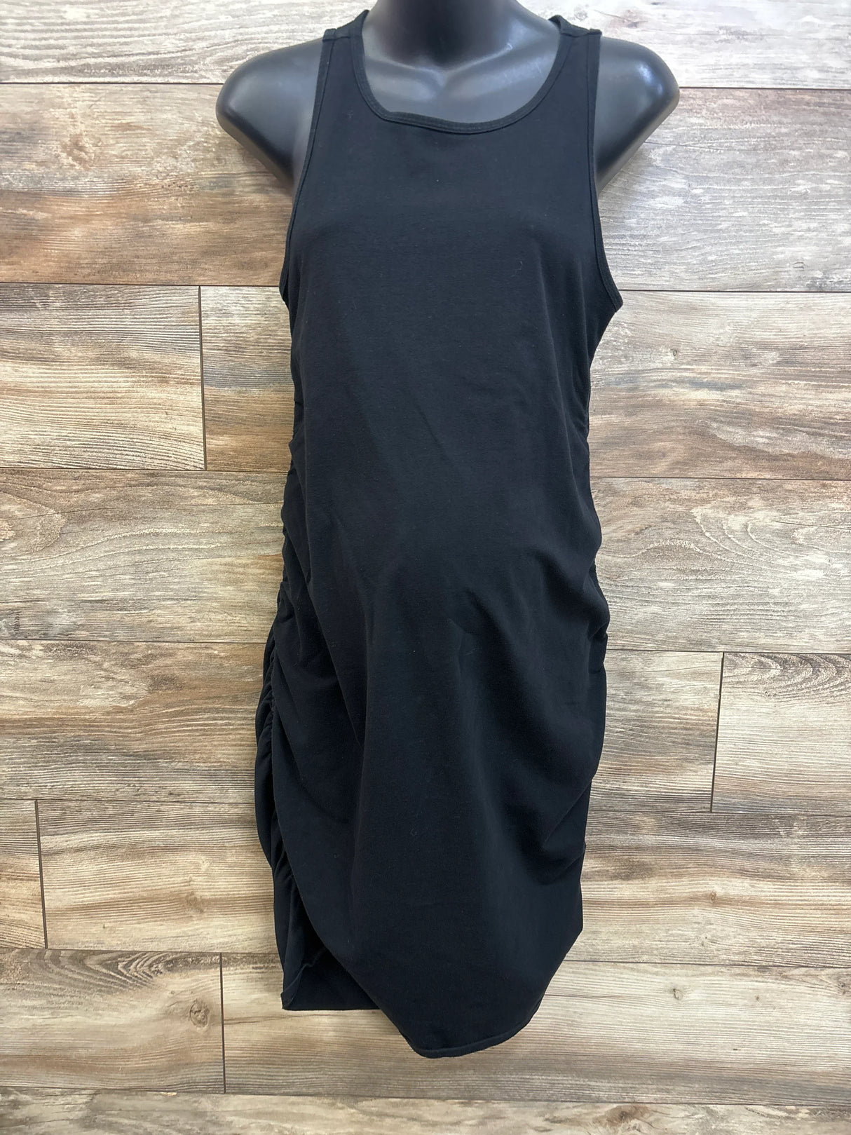 Front view of black Isabel maternity tank bodycon dress showing side ruching and scoop neckline on mannequin with wood background