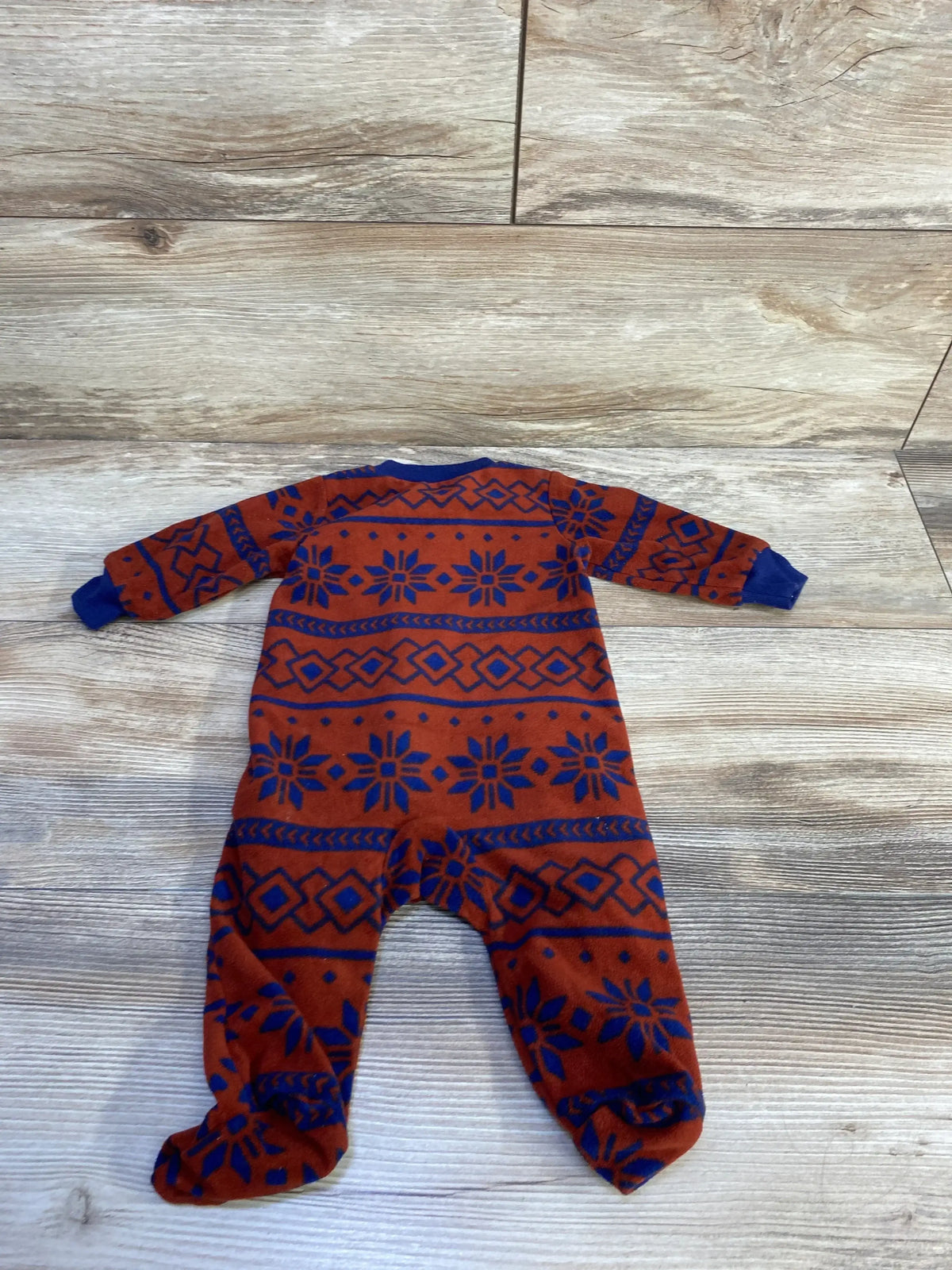 Flat back view of Carter’s rust blanket sleeper (3 months) showcasing blue snowflake and diamond pattern and footed legs on wood background