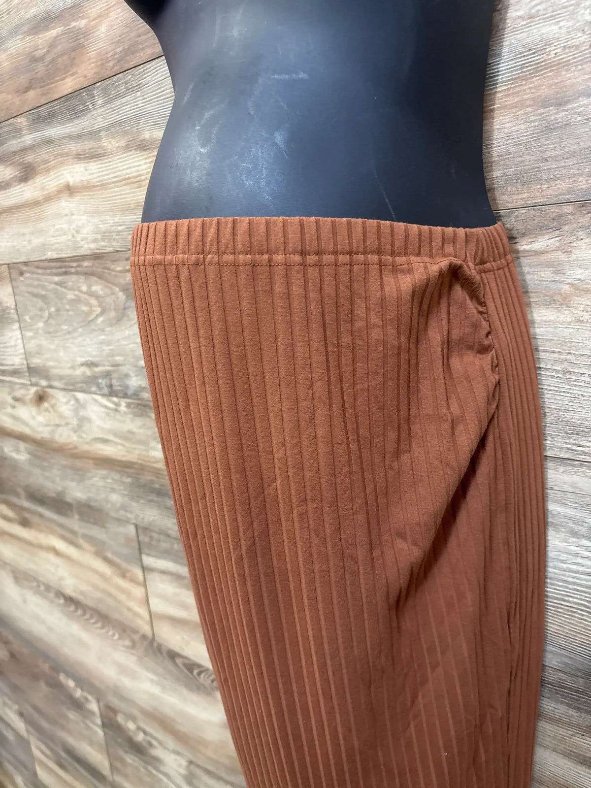 Side view of brown ribbed maternity skirt with elastic waistband on mannequin against wood background