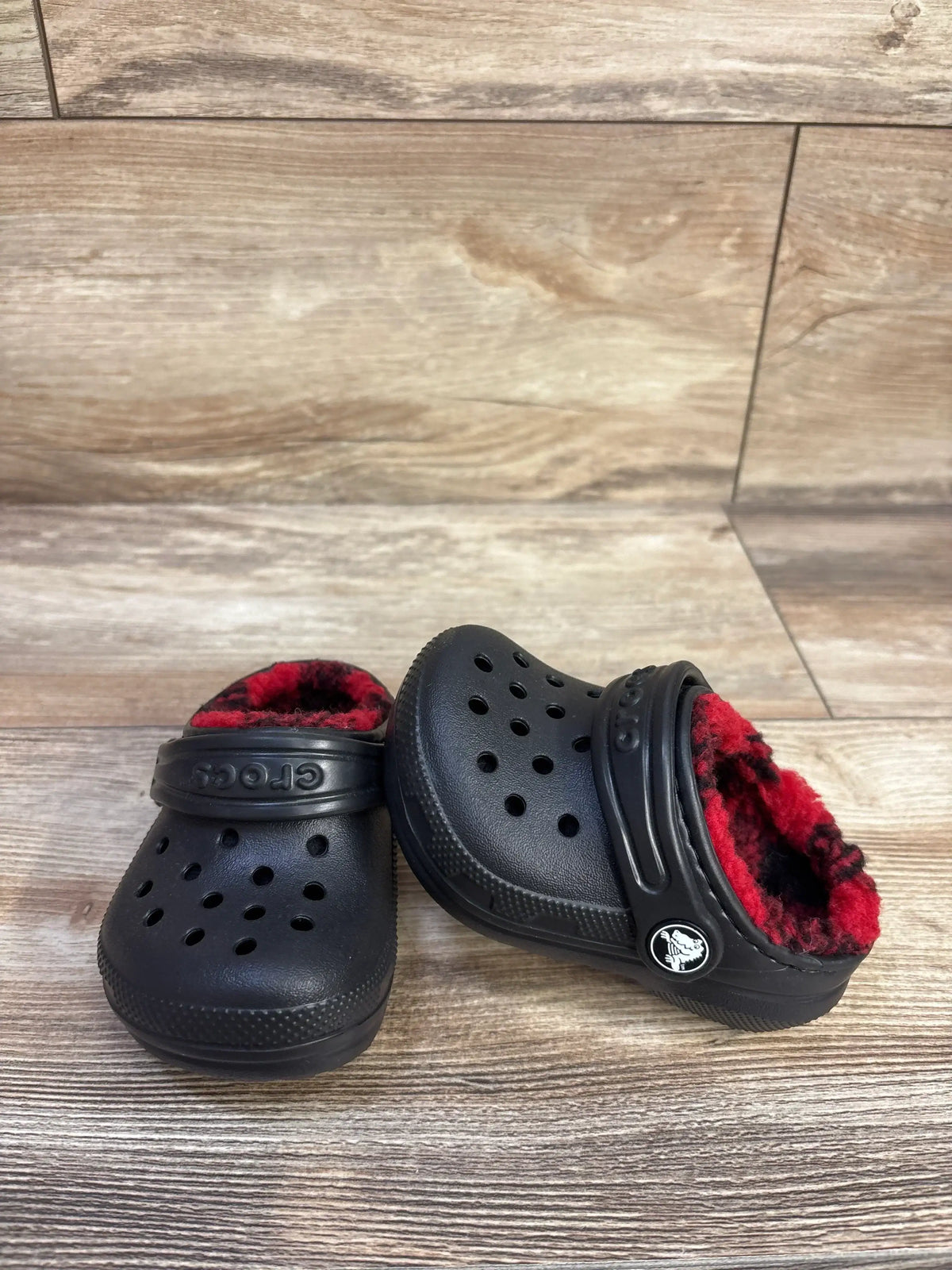 Three-quarter view of Crocs Classic clogs with red-black buffalo check lining and heel strap on wood floor