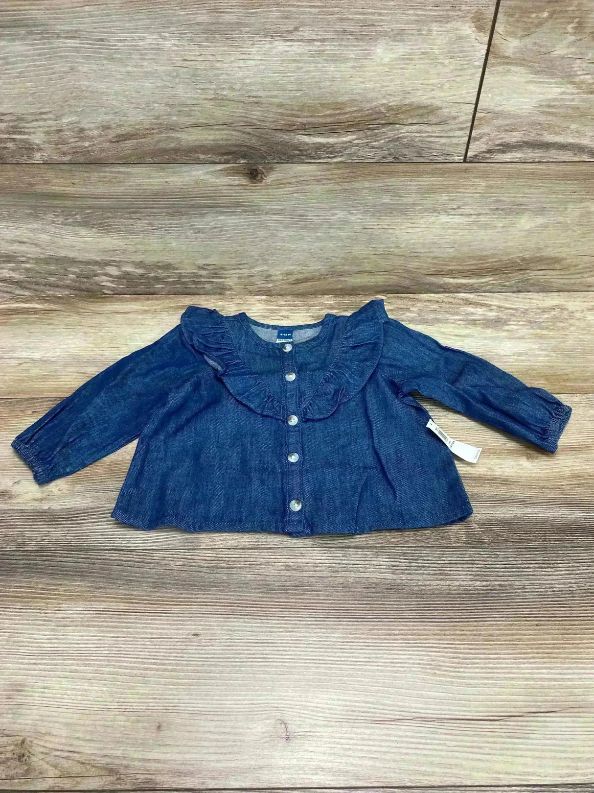 Front view of Old Navy denim top with ruffle collar and button front, long sleeves, laid flat on wood, size 6-12M