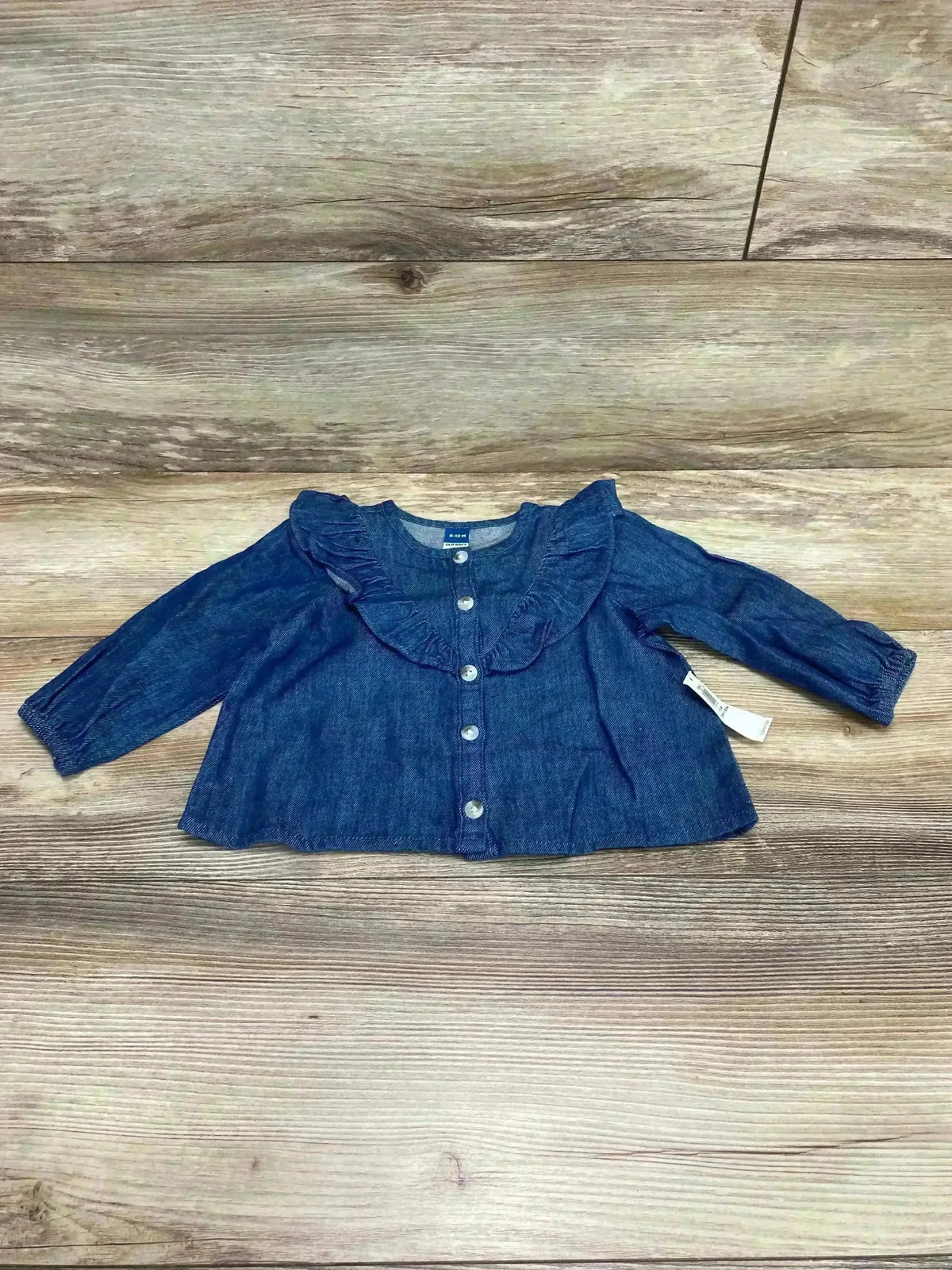 Front view of Old Navy denim top with ruffle collar and button front, long sleeves, laid flat on wood, size 6-12M