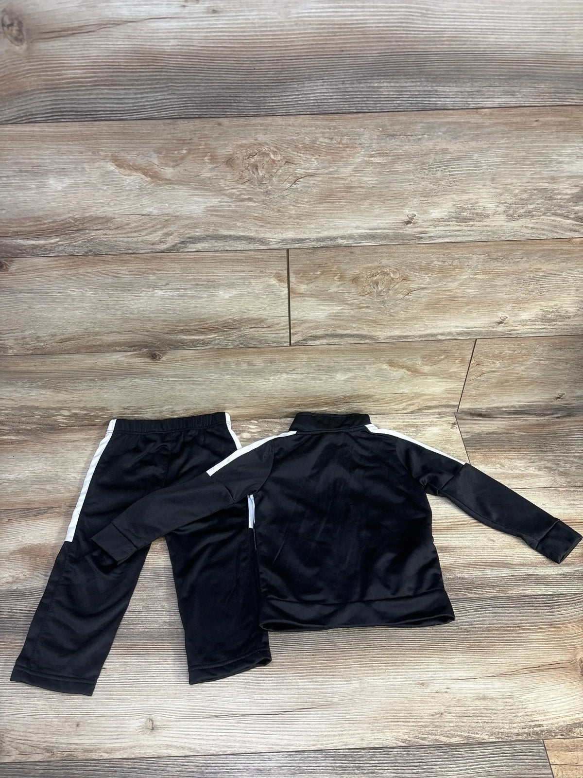 Flat lay of black Puma 2-piece tracksuit (24m) showing white side stripes and zip jacket on wood floor background
