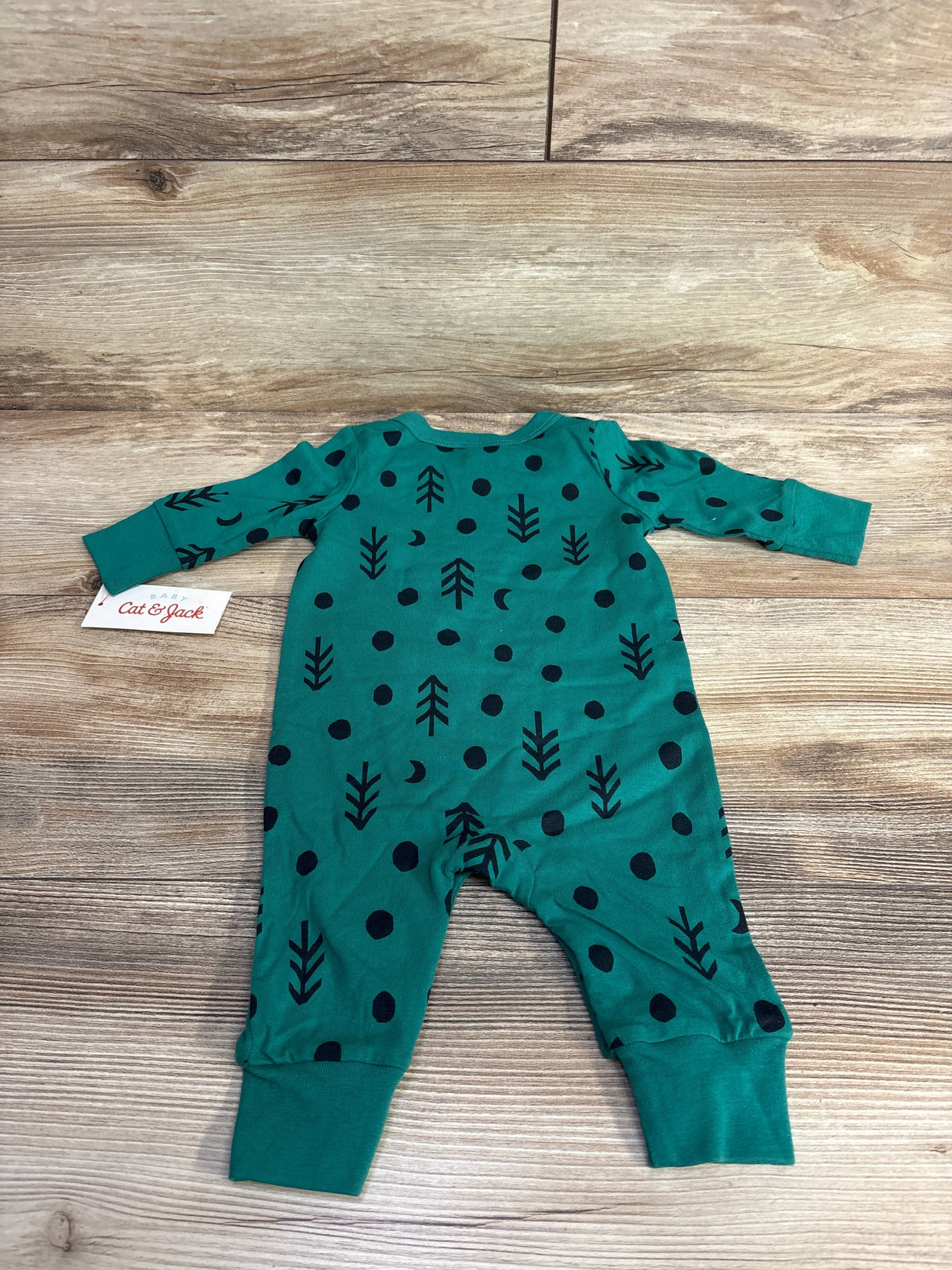 Green baby romper with black tree and dot pattern on wood floor