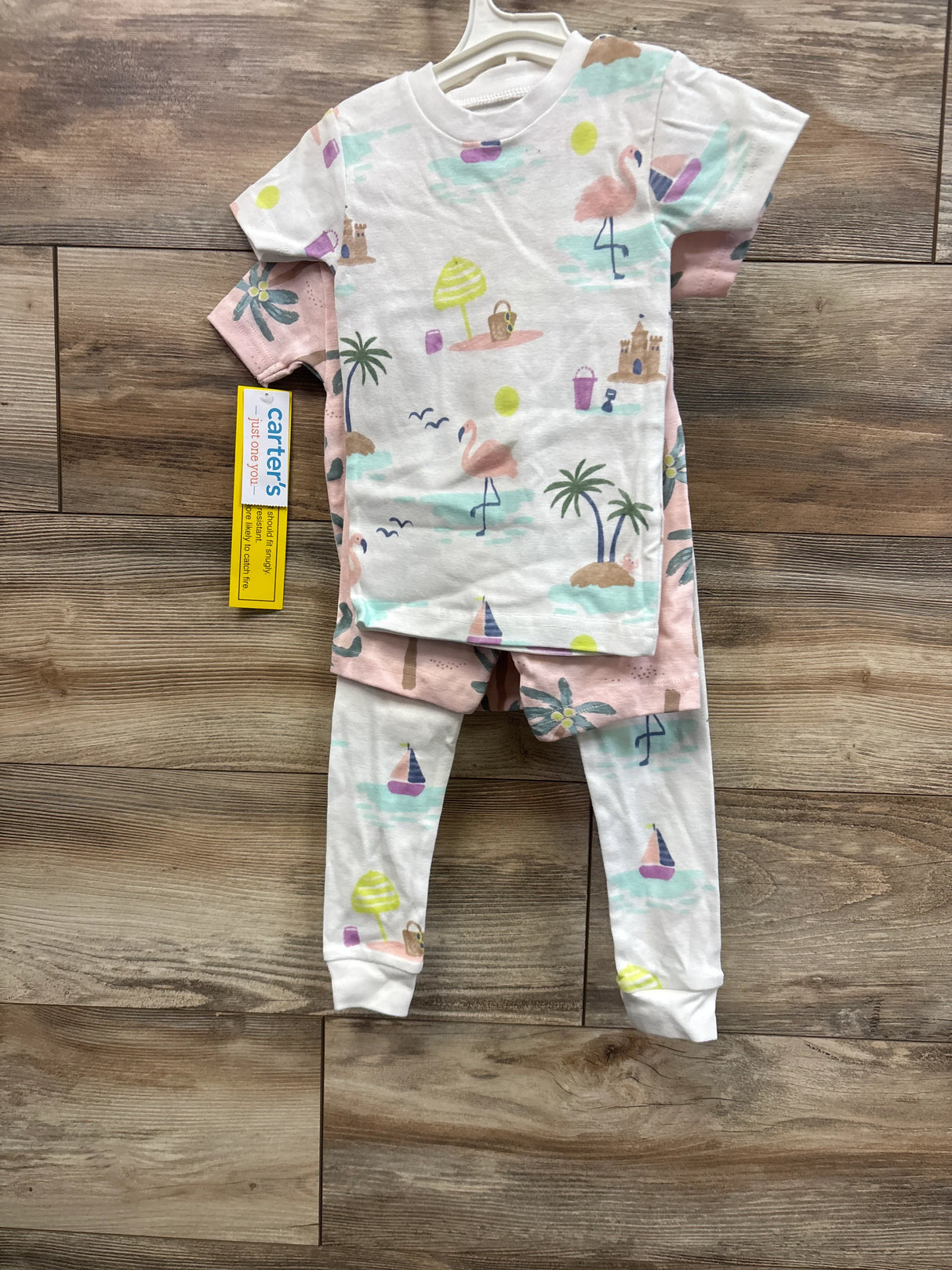 Flat lay of Just One You 4-piece toddler pajama set showcasing palm tree and flamingo beach print on wood floor
