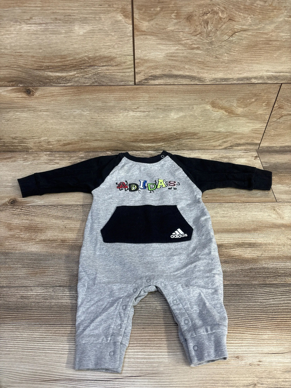 Front view of Adidas grey logo coverall, size 6 months, with black sleeves, front pocket, and snap closures