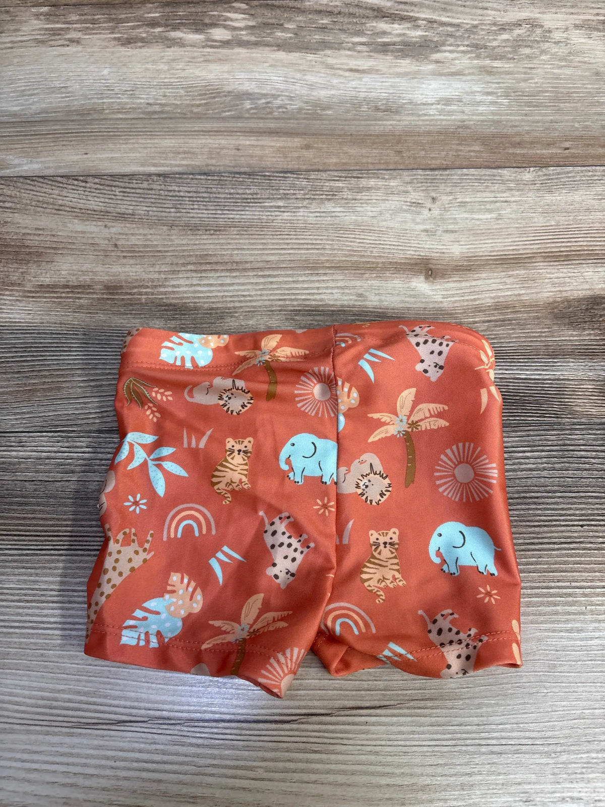 Front view of H&M orange animal print swim shorts showcasing elastic waistband with wood-grain background