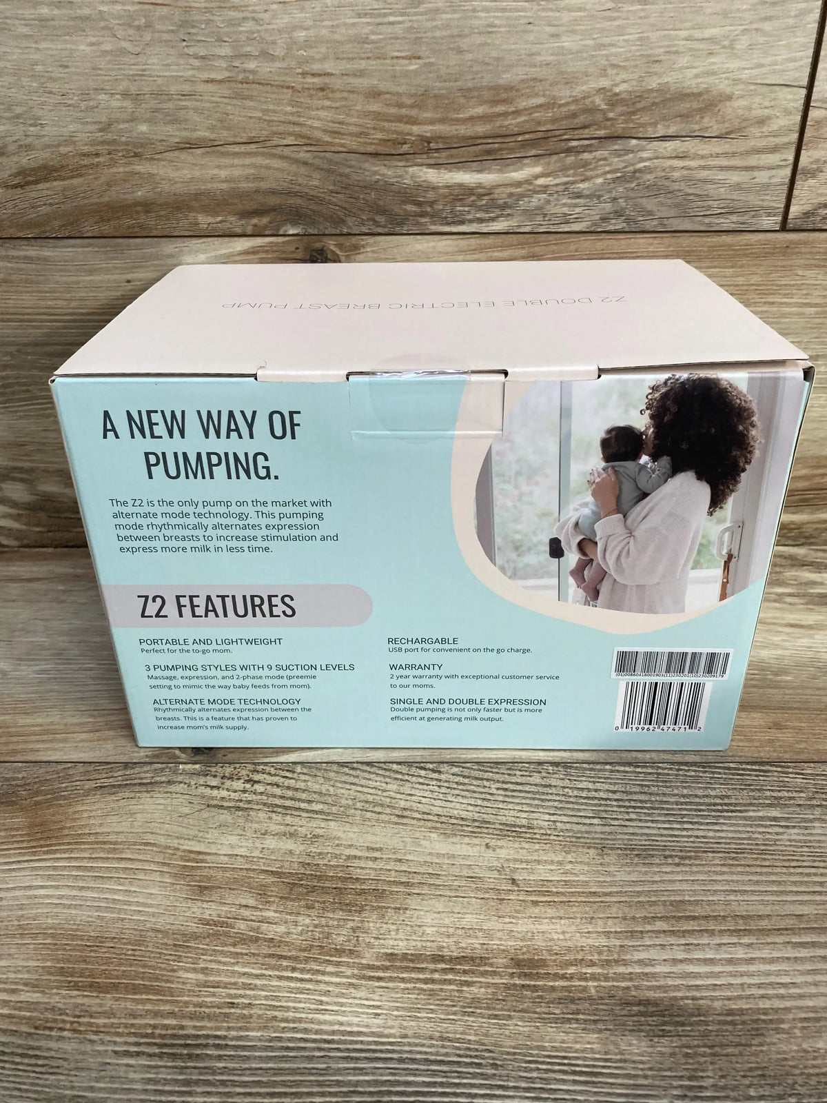 Front of Zomee Z2 double electric breast pump box showcasing headline ‘A NEW WAY OF PUMPING’ and photo of a mother holding a baby on a wood table