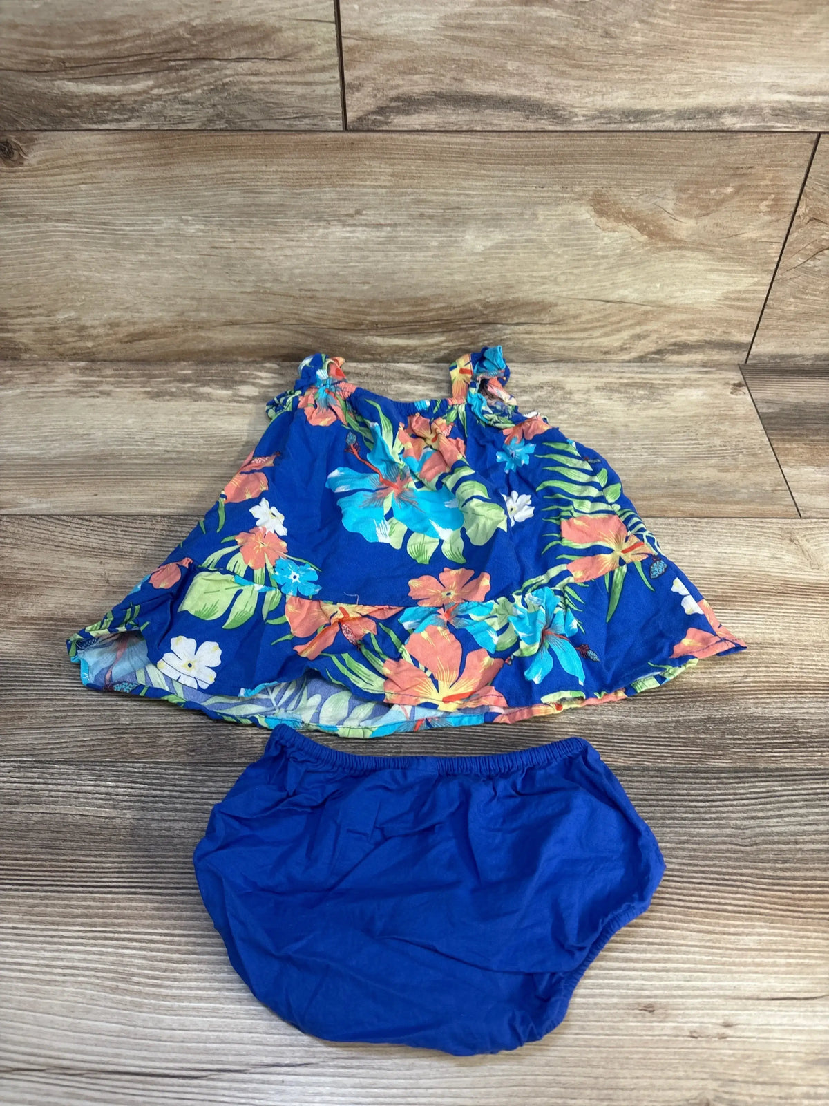 Flat lay of Children's Place blue floral baby dress with ruffled shoulder straps and matching blue bloomers on wooden background