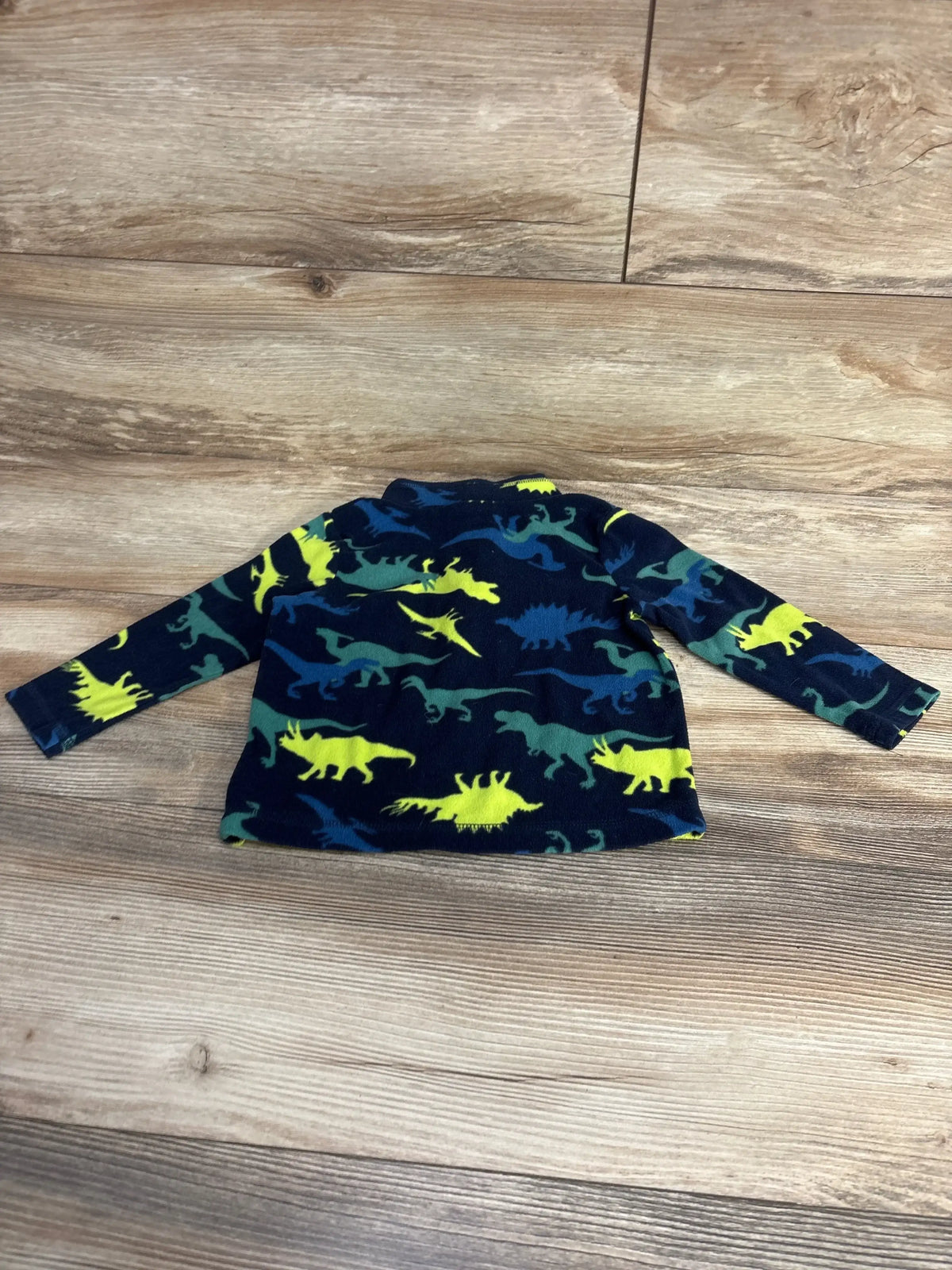 Children's fleece jacket with multicolored dinosaur print on wooden floor background