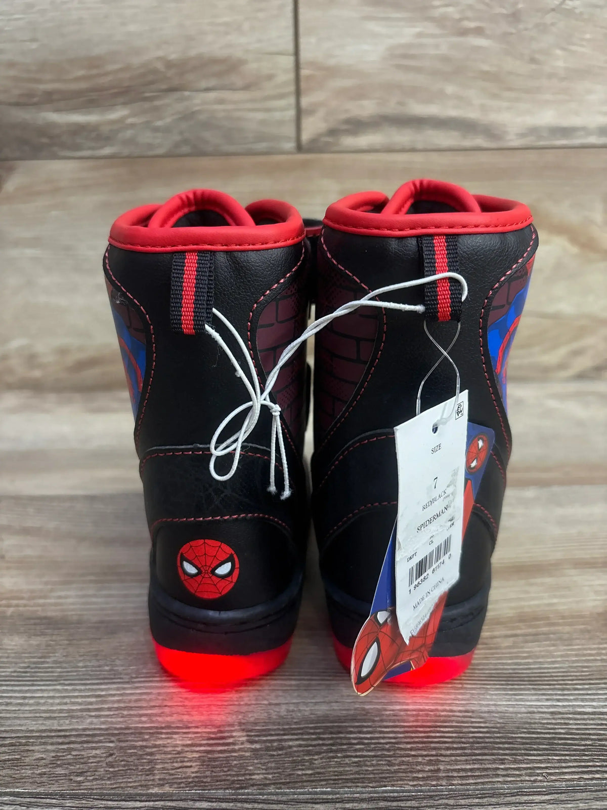 Kids' black and red Spider-Man light-up boots with character face and tag, shown on wood floor.