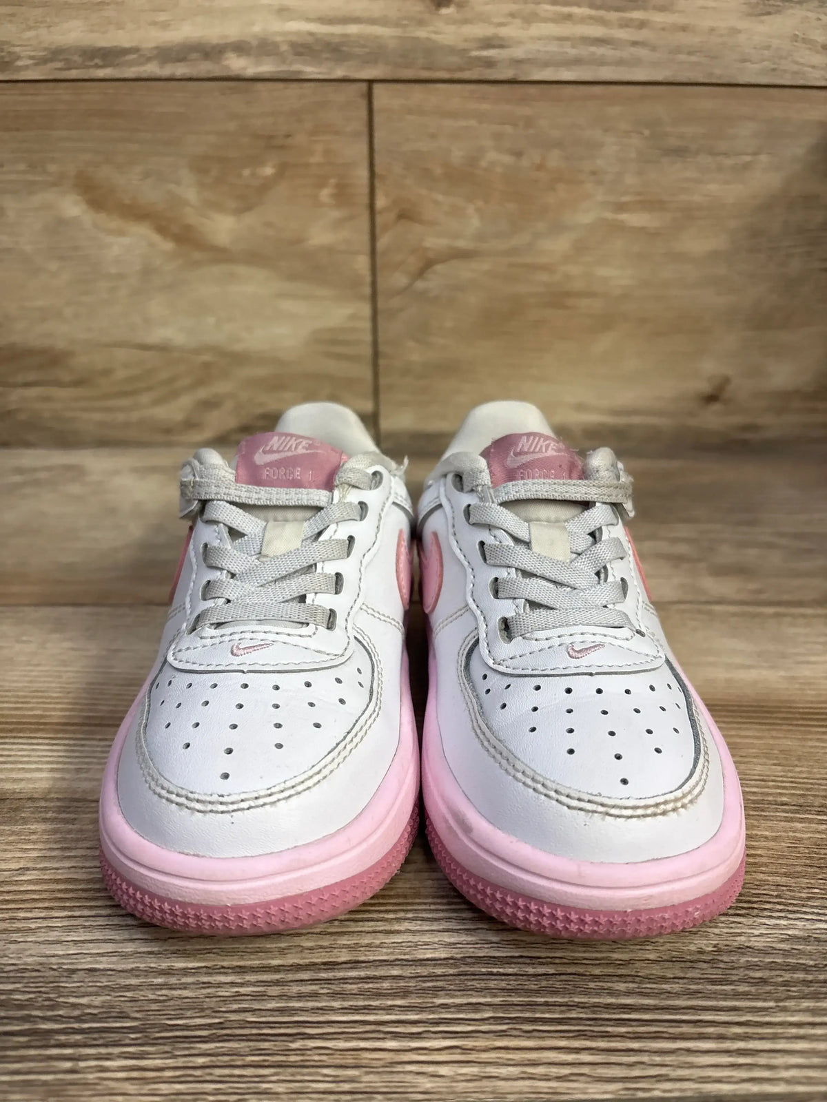 Front view of Nike Air Force 1 Low EasyOn sneakers showing white leather with pink accents and pink sole on wooden floor